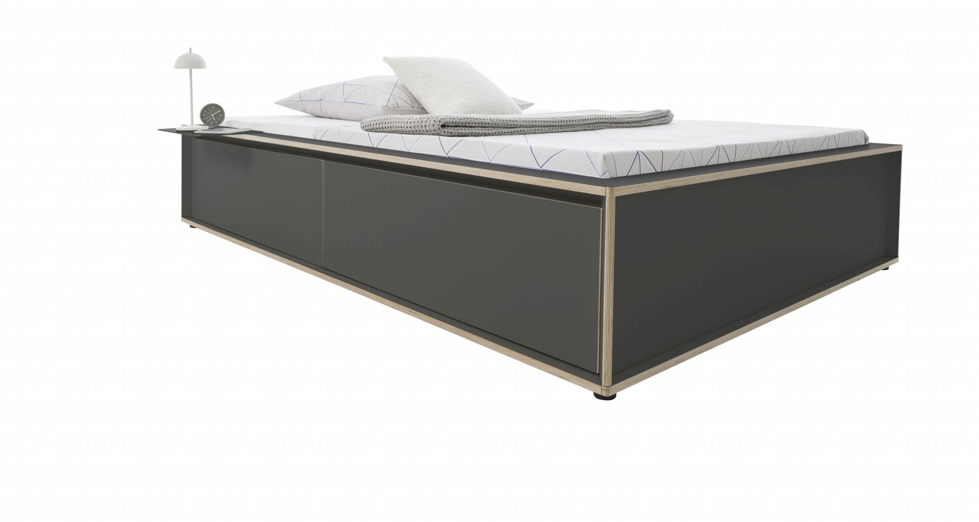 Spaze Bett von Müller Möbelwerkstätten in Grau mit Nachttisch, Lampe, Kissen und Decke.
