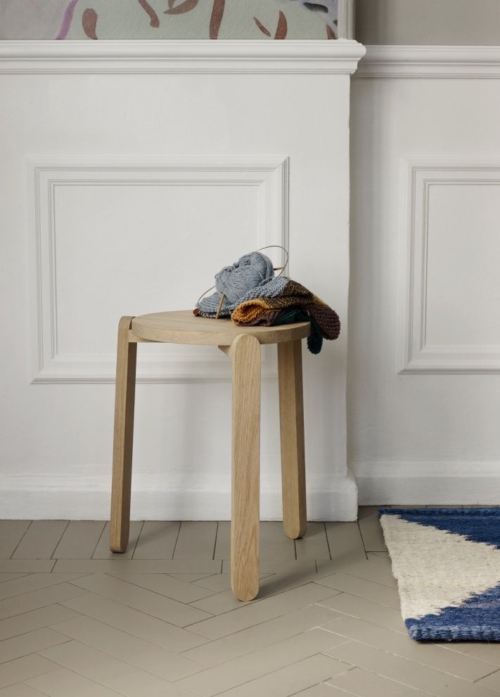 Nomad Hocker von Skagerak: Heller Holz-Hocker mit Strickzeug vor weißer Wand. Modernes Möbeldesign.