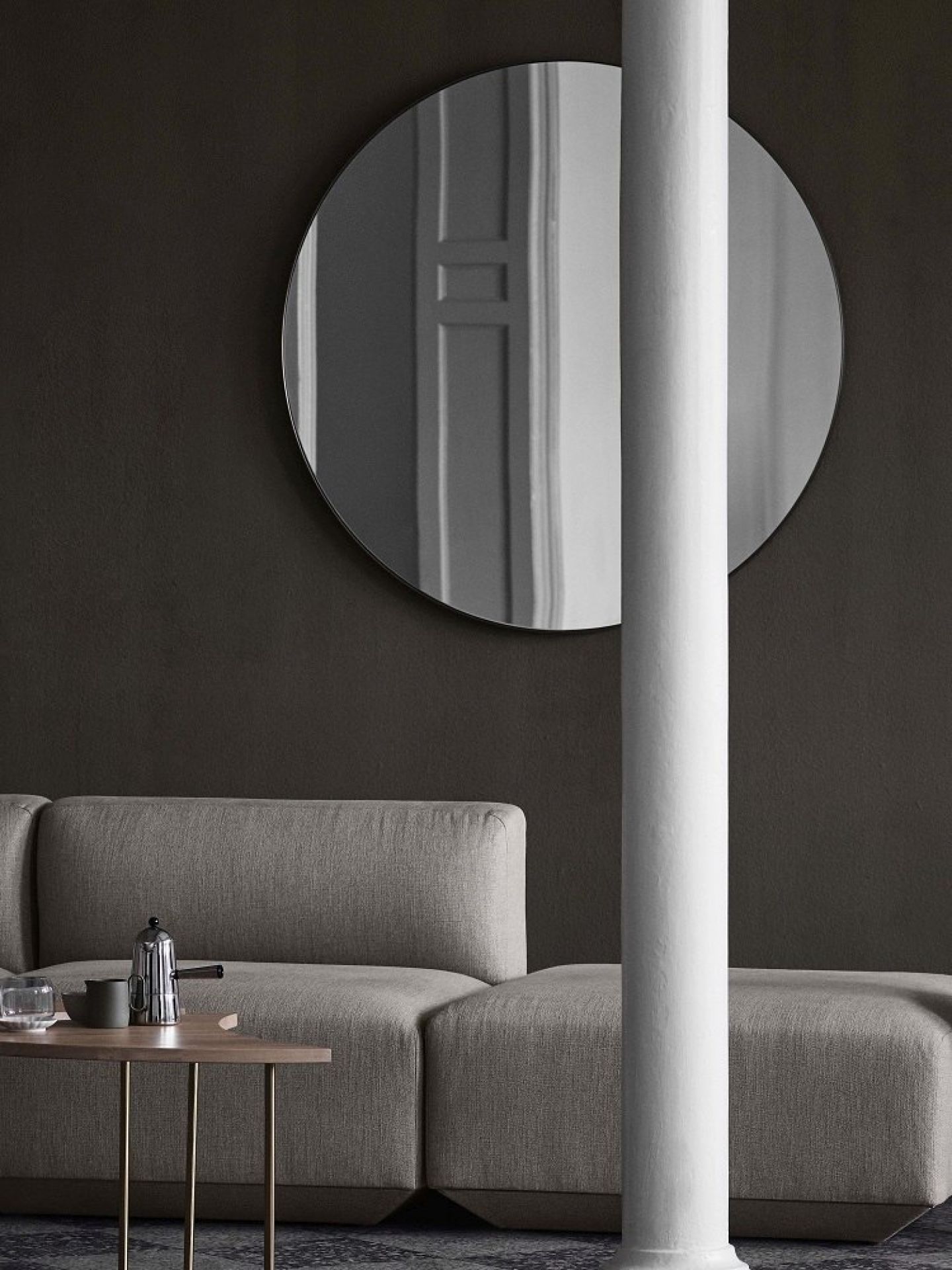 AndTradition Pinwheel HM7 Beistelltisch neben Sofa mit Kaffeekanne und rundem Spiegel an dunkler Wand.