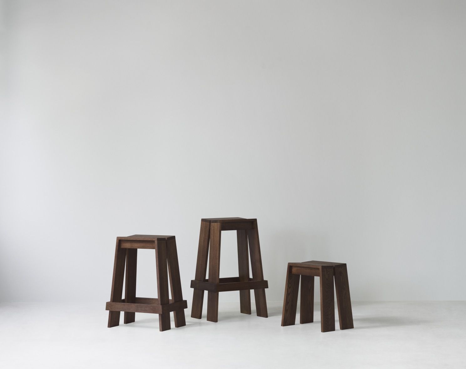 Drei braune Let Barhocker von Normann Copenhagen in verschiedenen Höhen vor einer weißen Wand.