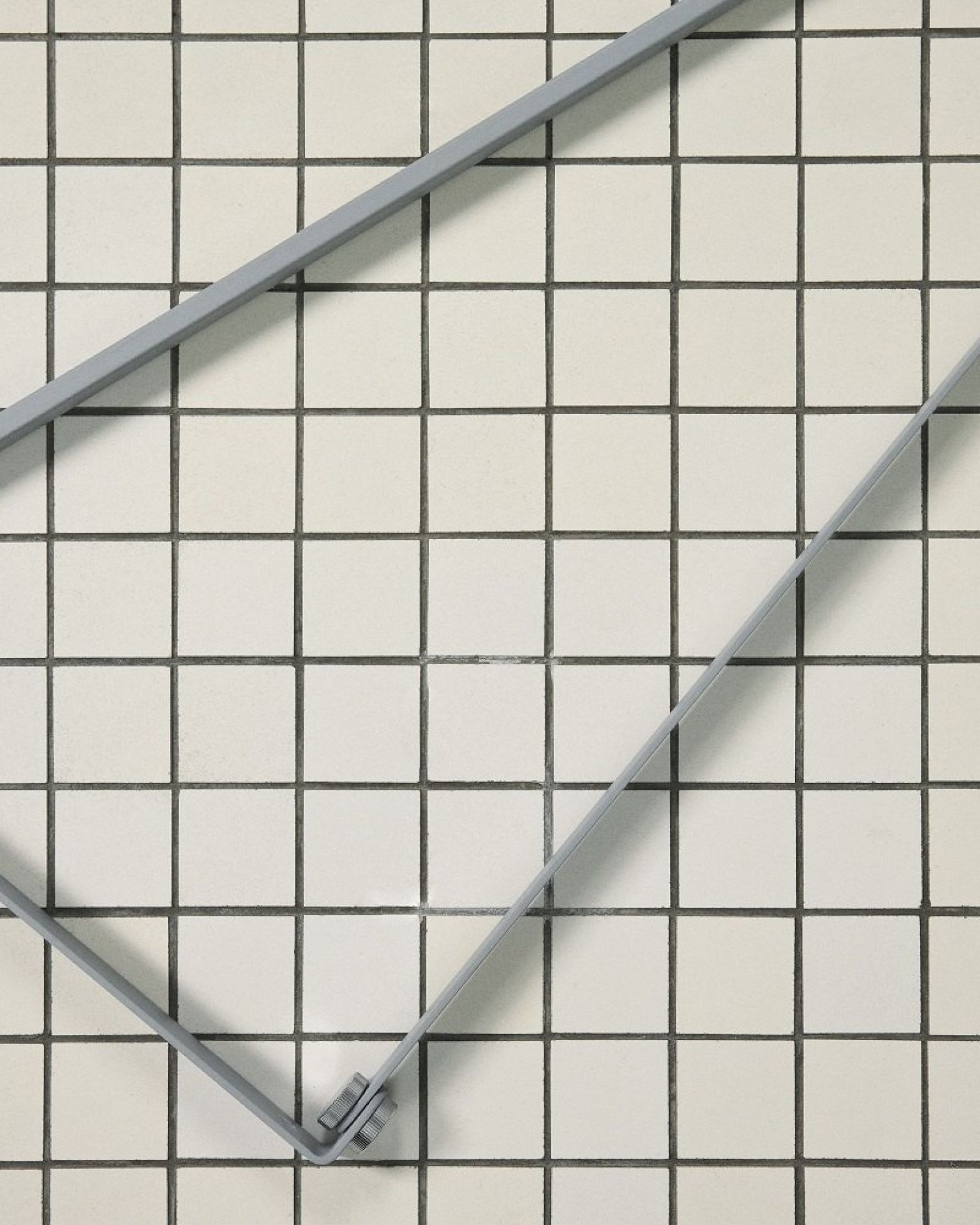 Detailaufnahme der 265 Chromatica Wandleuchte von Flos vor einem Hintergrund aus weißen quadratischen Fliesen.