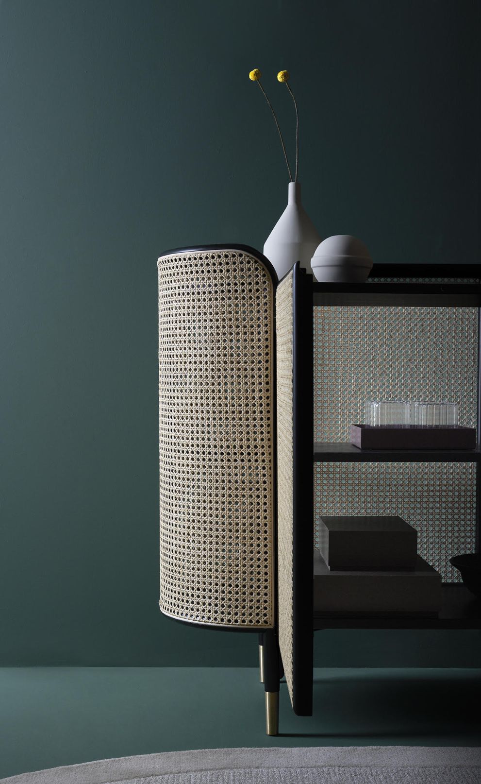 MOS CABINET Schrank von Wiener GTV Design mit Wiener Geflecht und schwarzen Akzenten vor dunkelgrünem Hintergrund.