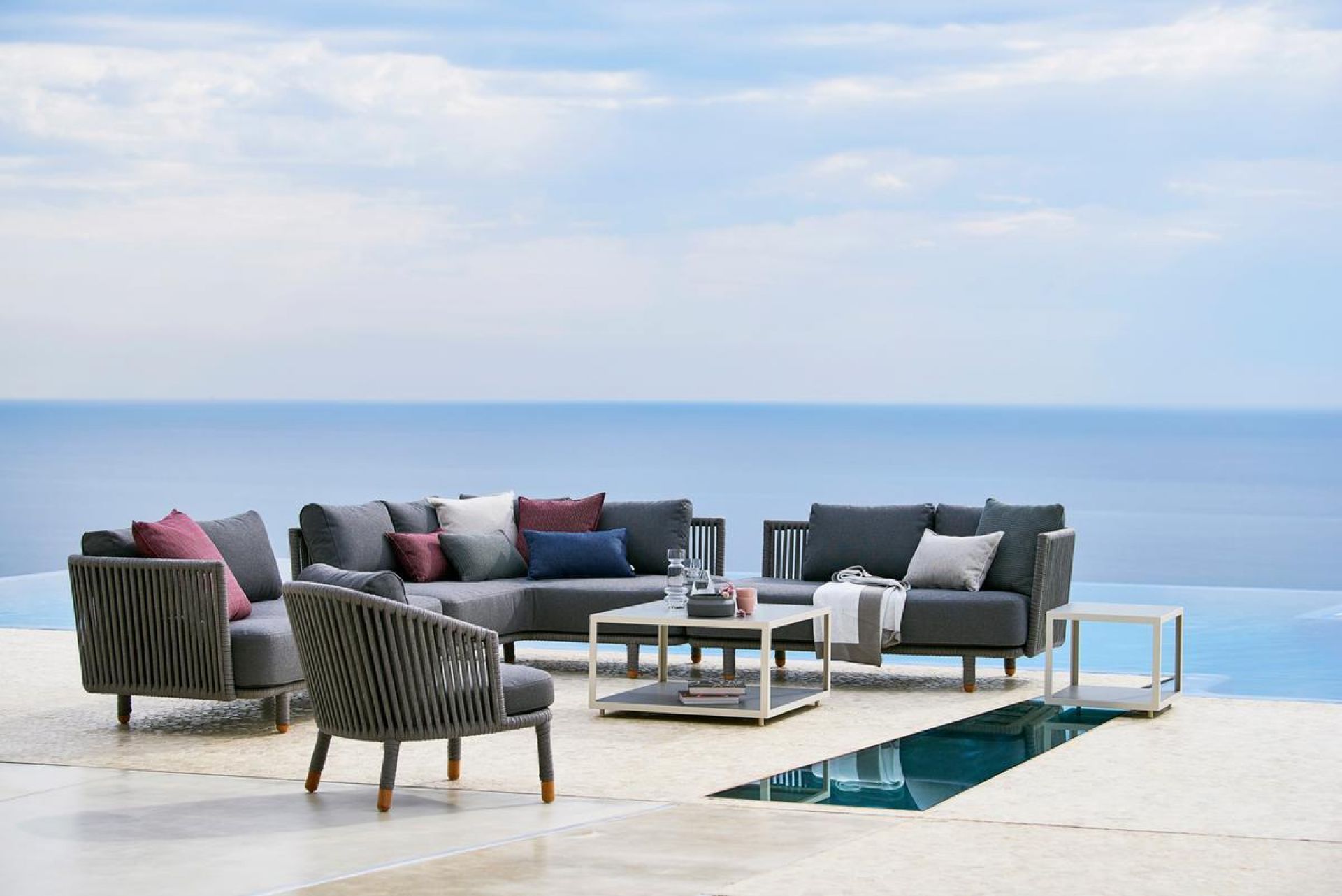 Cane-Line Moments Lounge Sessel und Outdoor-Sofa mit Kissen vor Meerblick. Gartenmöbel aus Rattan.