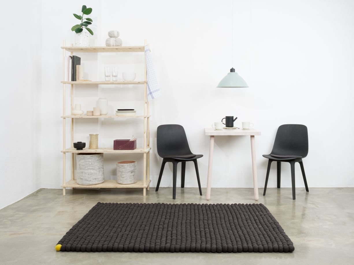 Anthrazitfarbener Filzteppich "Big One" von myfelt (140x200 cm) im modernen Wohnraum mit Regalen und Stühlen.