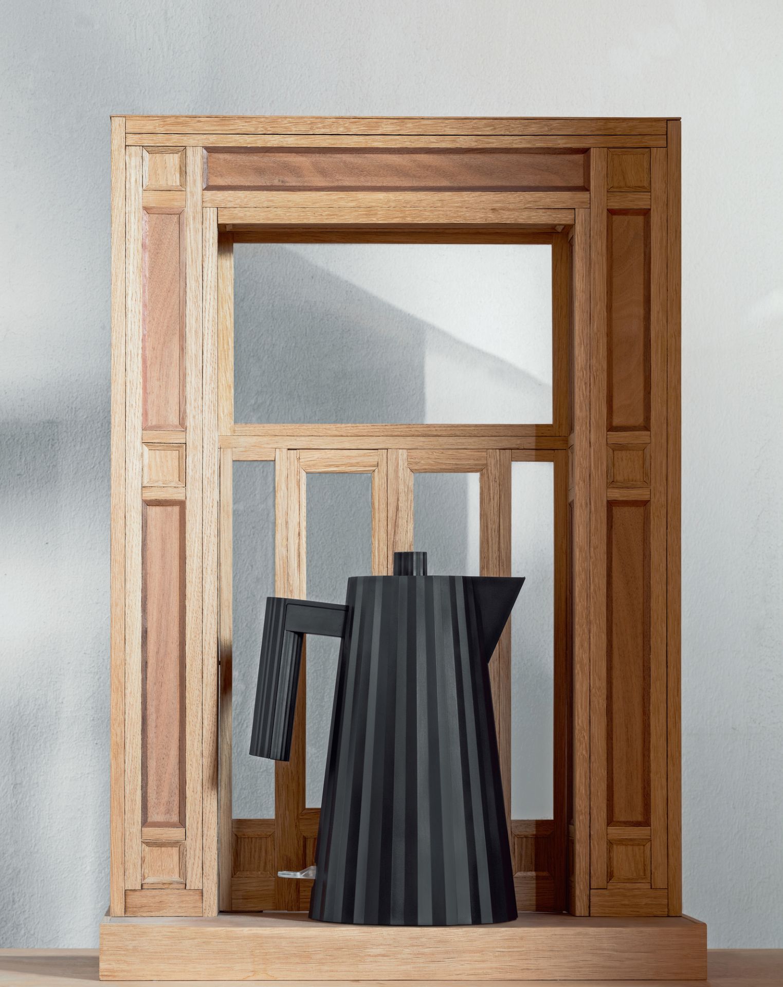 Grauer Alessi MDL06 Plissé Wasserkocher vor Holzrahmen, modernes Küchendesign.
