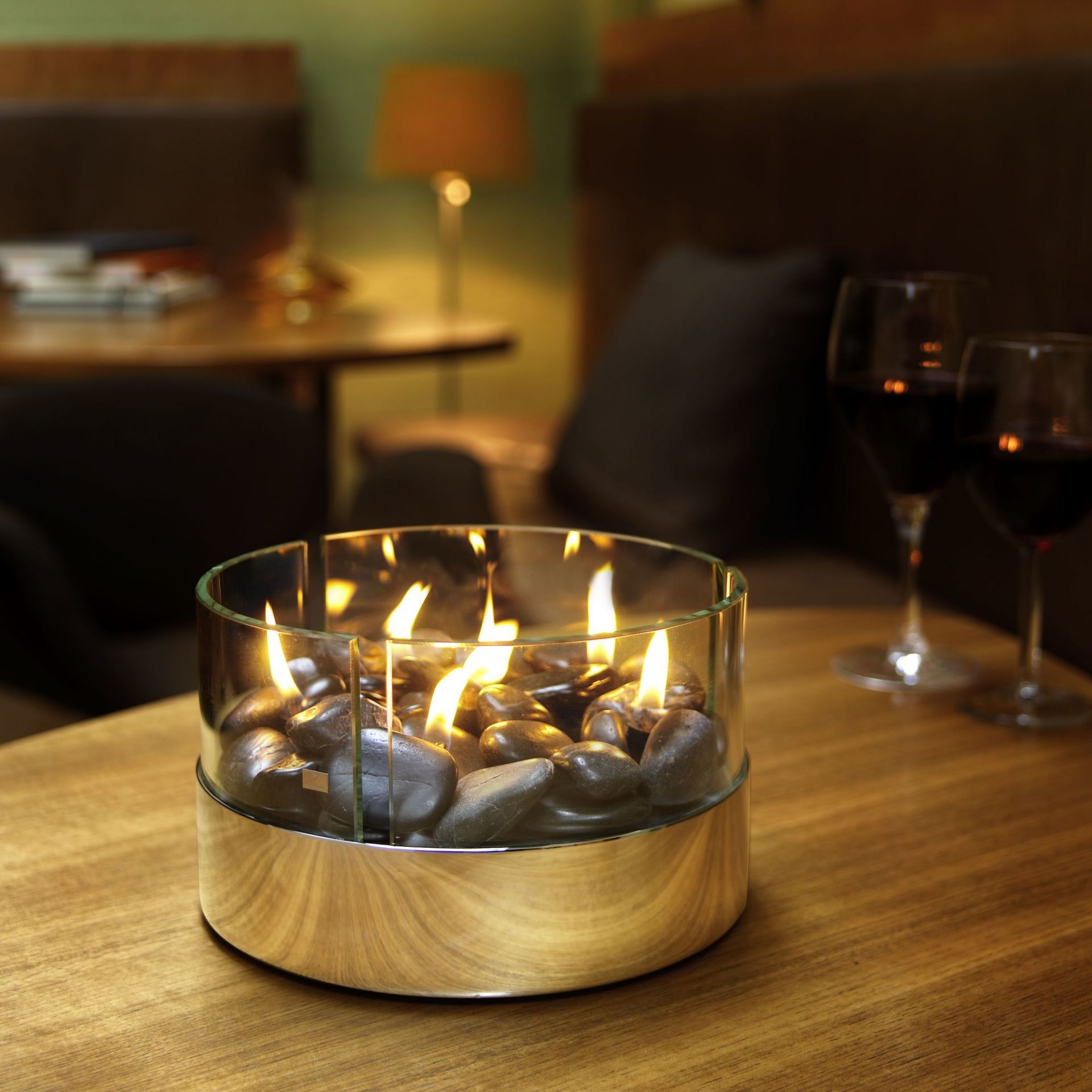 Philippi Burn Tischkamin mit Steinen und Flammen in Glasbehälter auf einem Holztisch.