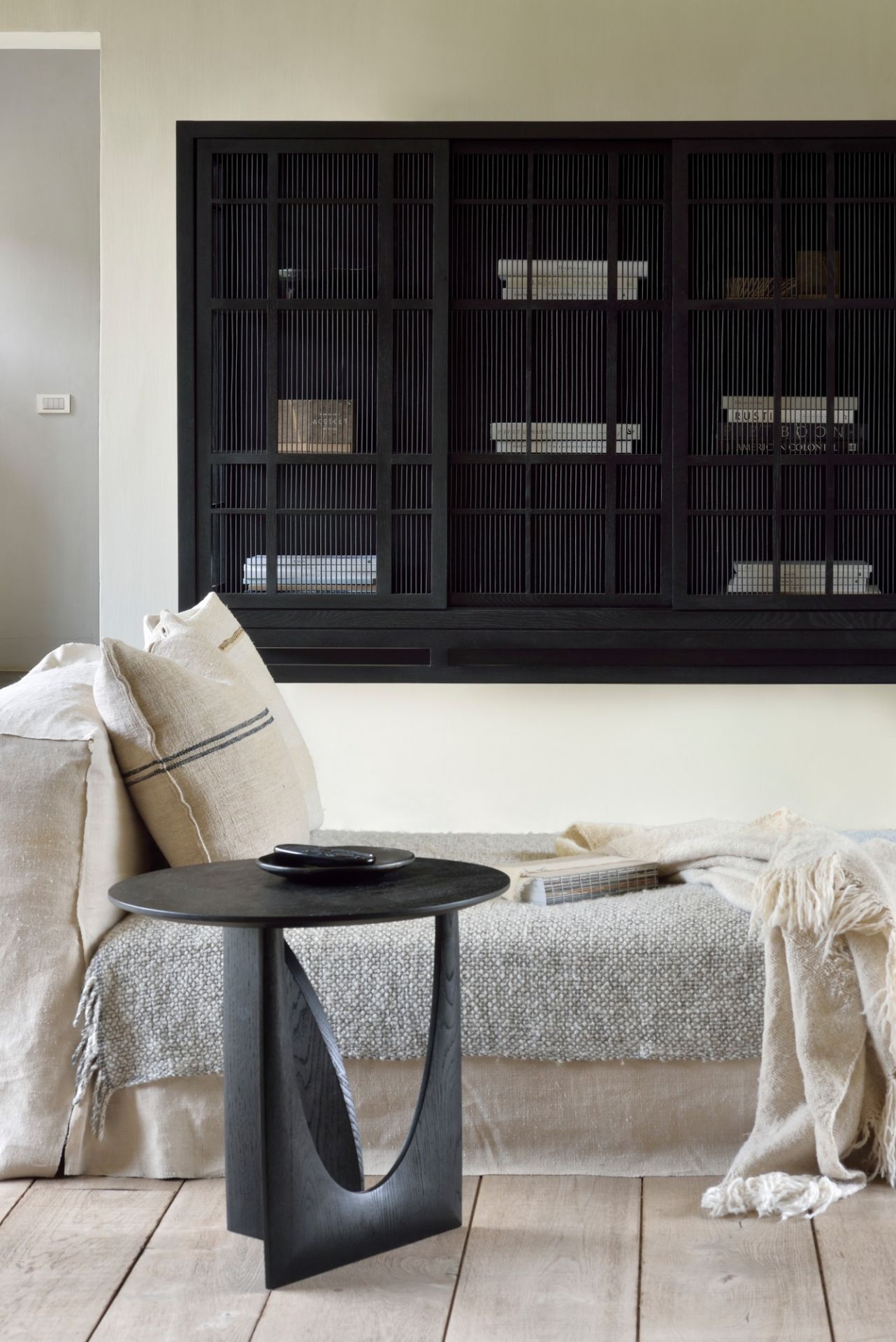 Schwarzer Ethnicraft Beistelltisch aus Eiche mit geometrischem Design neben einem Sofa im Wohnzimmer.