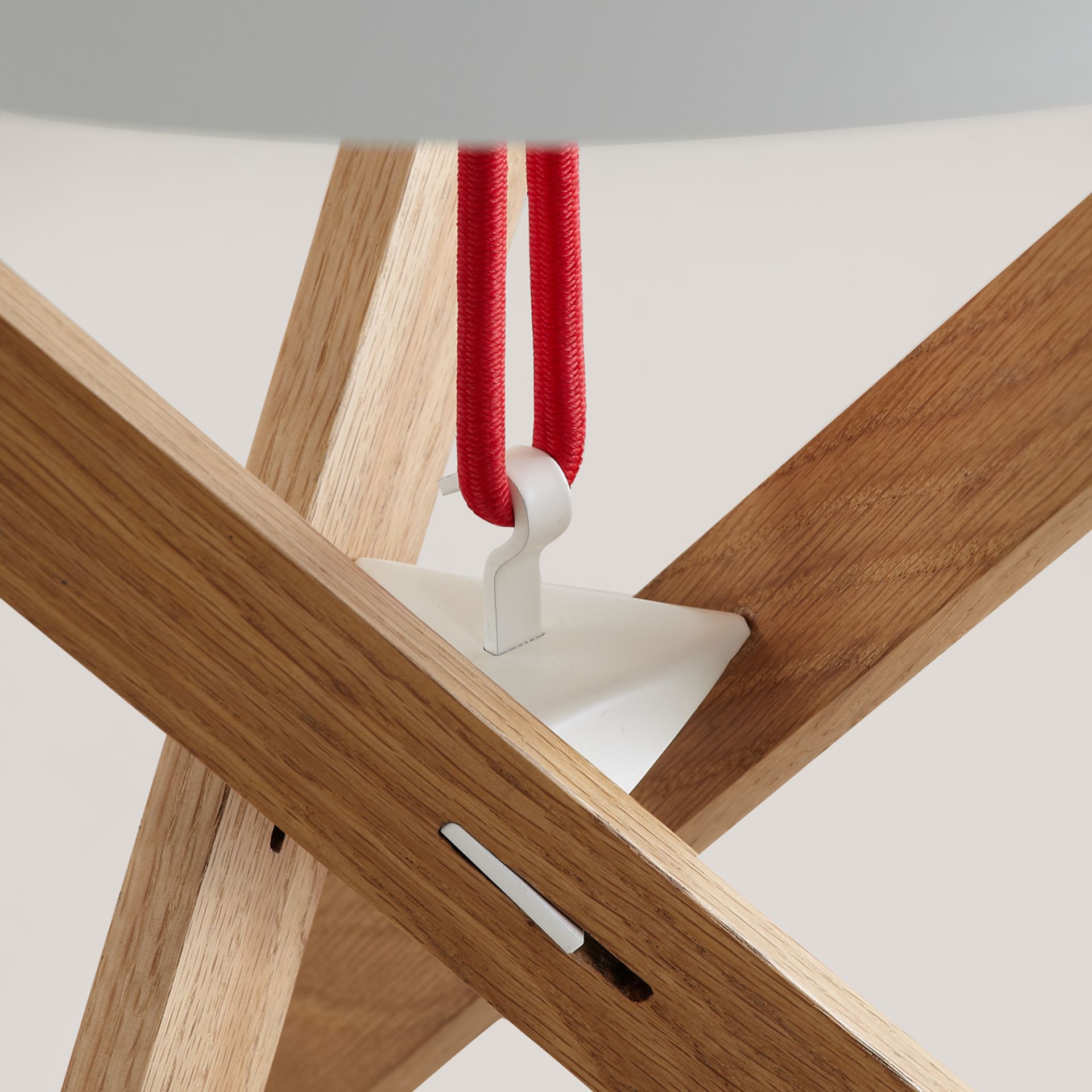 Detailaufnahme des Mox Marionet Beistelltisches: Holzgestell mit roter Zuleitung und weißer Halterung.