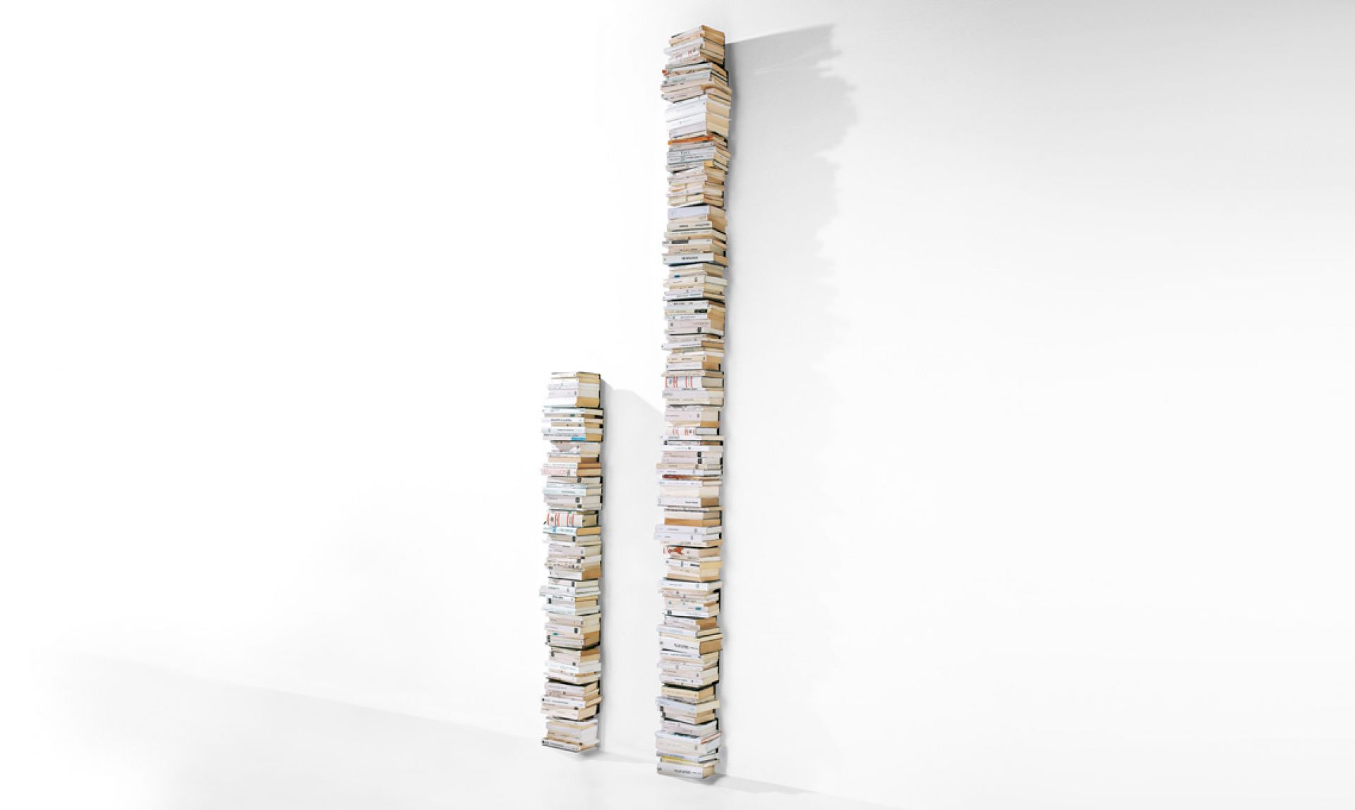Ptolomeo Wall Büchersäule von Opinion Ciatti: Zwei vertikale Bücherstapel an einer weißen Wand.