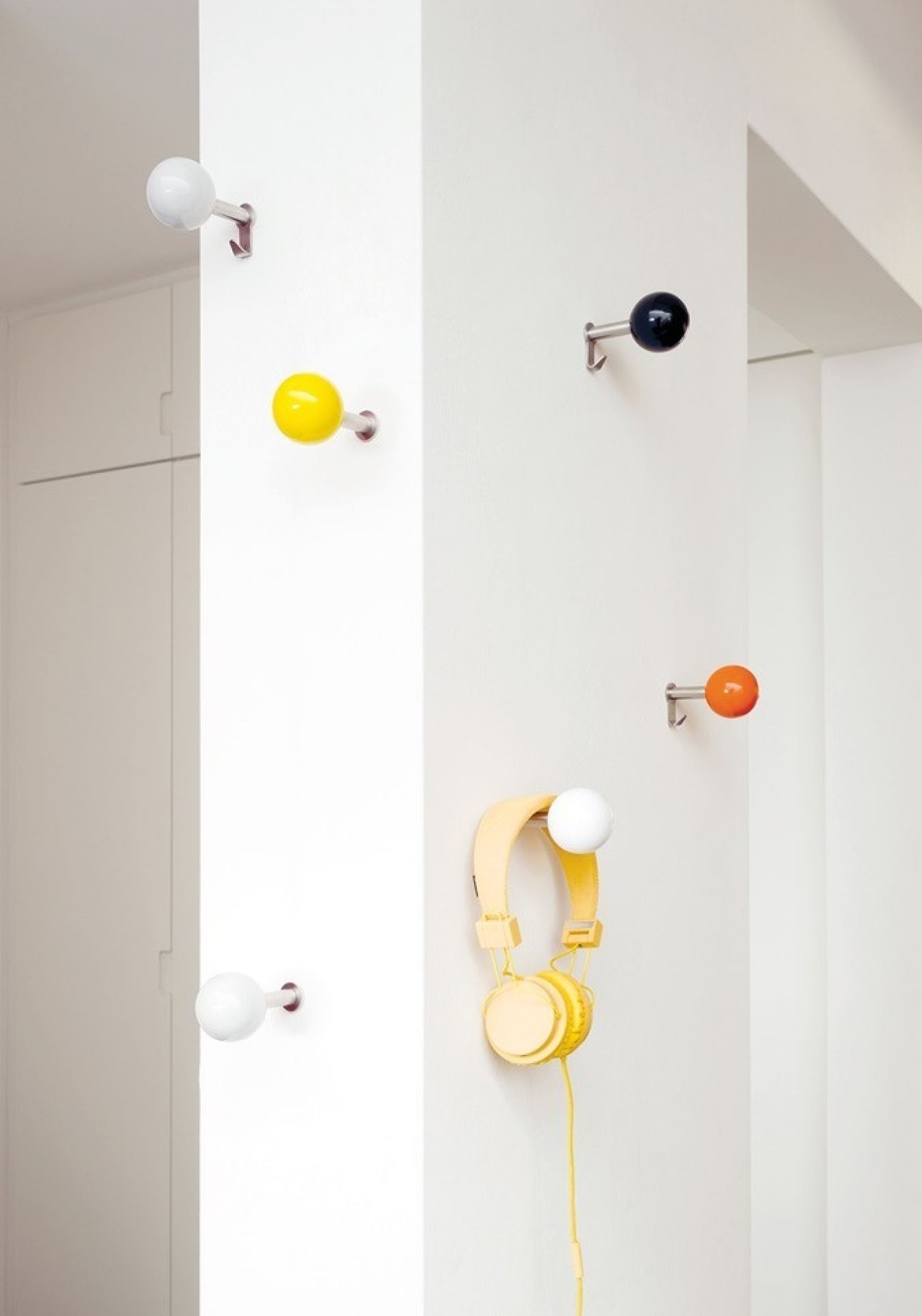 Dots Wandhaken von Schönbuch: Fünf farbenfrohe Garderobenhaken an einer weißen Wand, einer mit Kopfhörern.