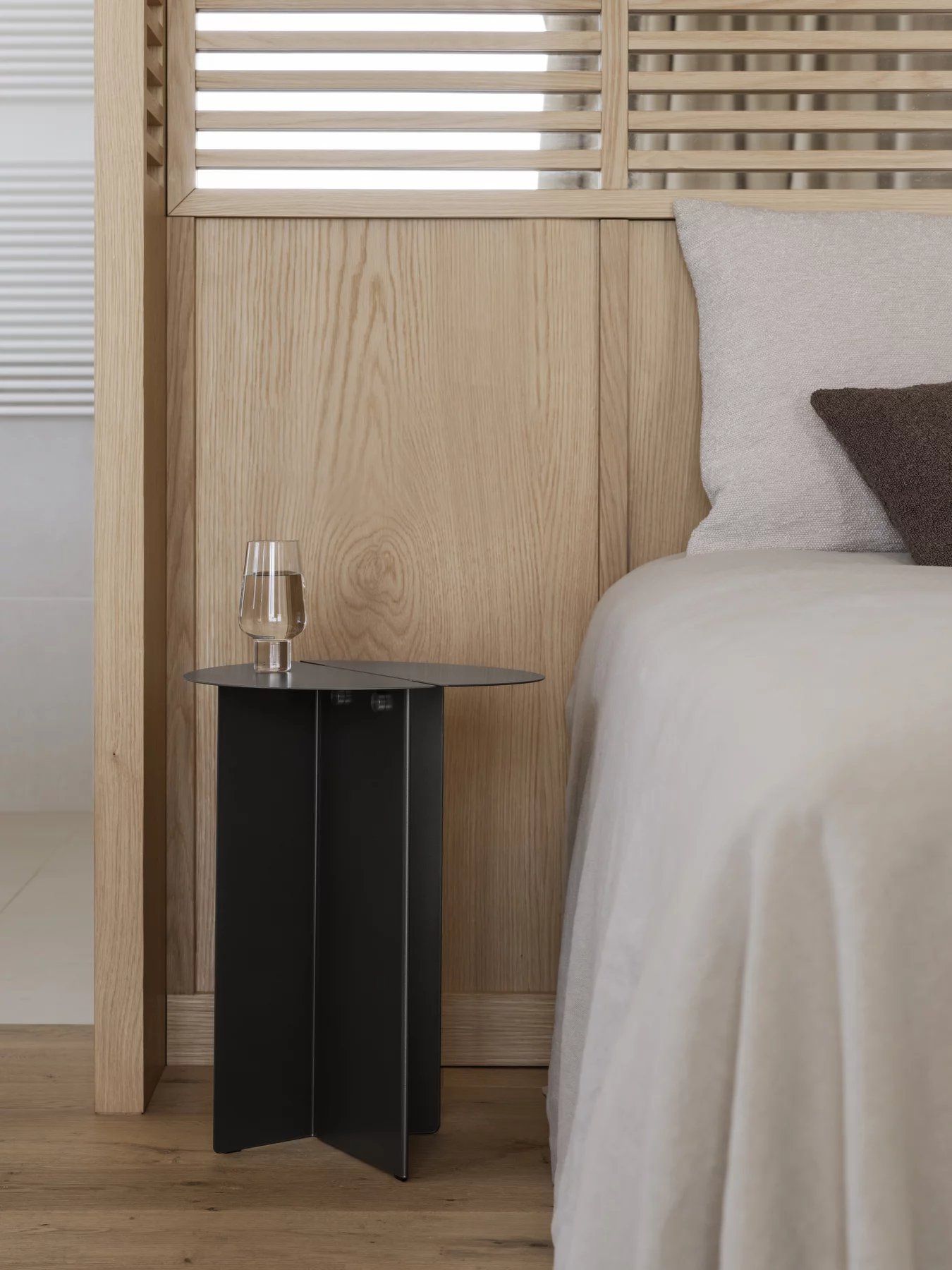 Oru Beistelltisch von Blomus in Burned Metal neben einem Bett. Moderner Nachttisch mit metallischem Finish.