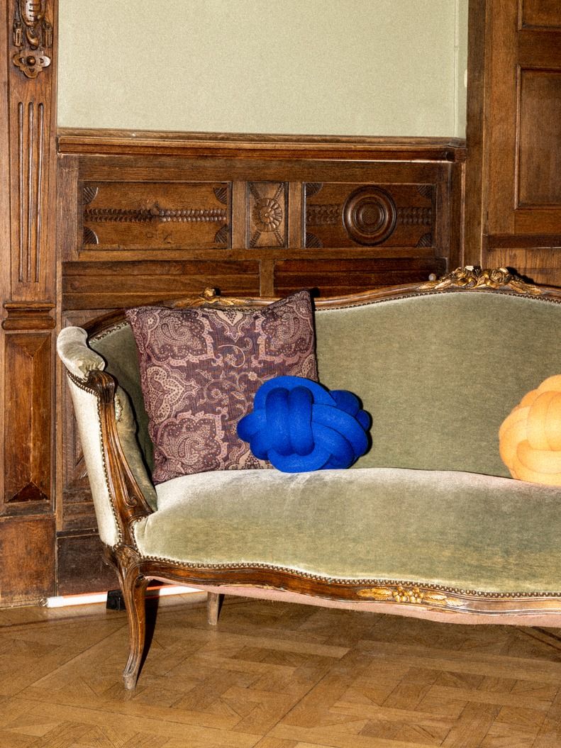 Blaues Knot Kissen von Design House Stockholm auf einem grünen Sofa mit Musterkissen.