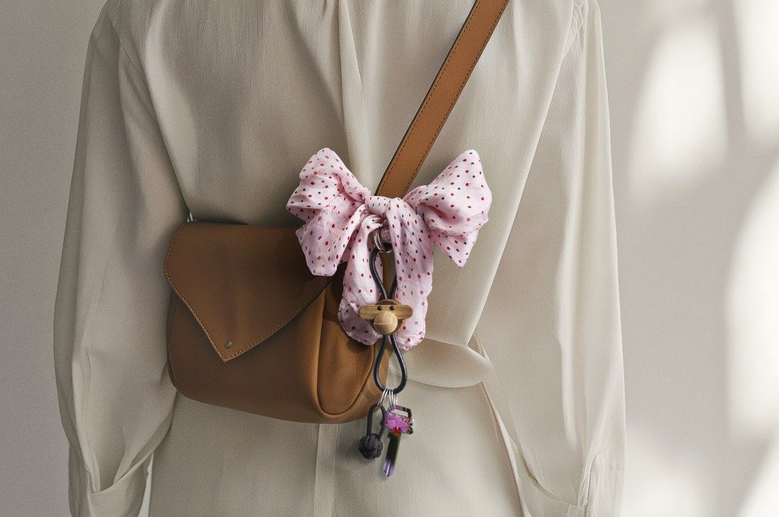 Kay Bojesen Affe Schlüsselanhänger aus Holz und Leder an brauner Handtasche mit Schleife.