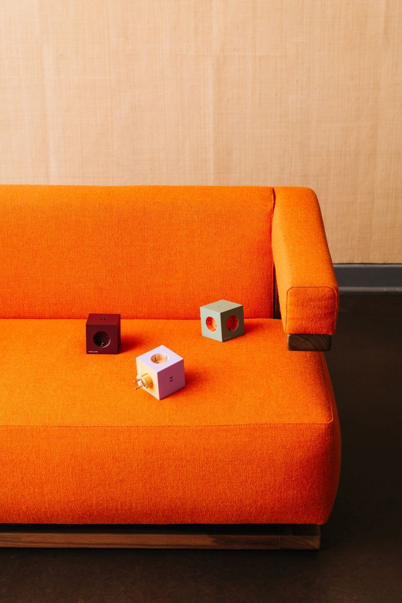 Drei Avolt Square 2 Steckdosenwürfel in Rot, Lila und Grün auf einem orangefarbenen Sofa.