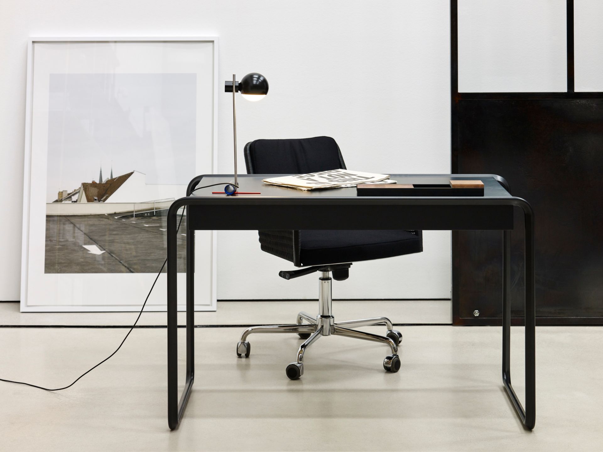 L25 Tischleuchte von Tecta auf schwarzem Schreibtisch mit Bürostuhl und minimalistischer Dekoration im modernen Büro.