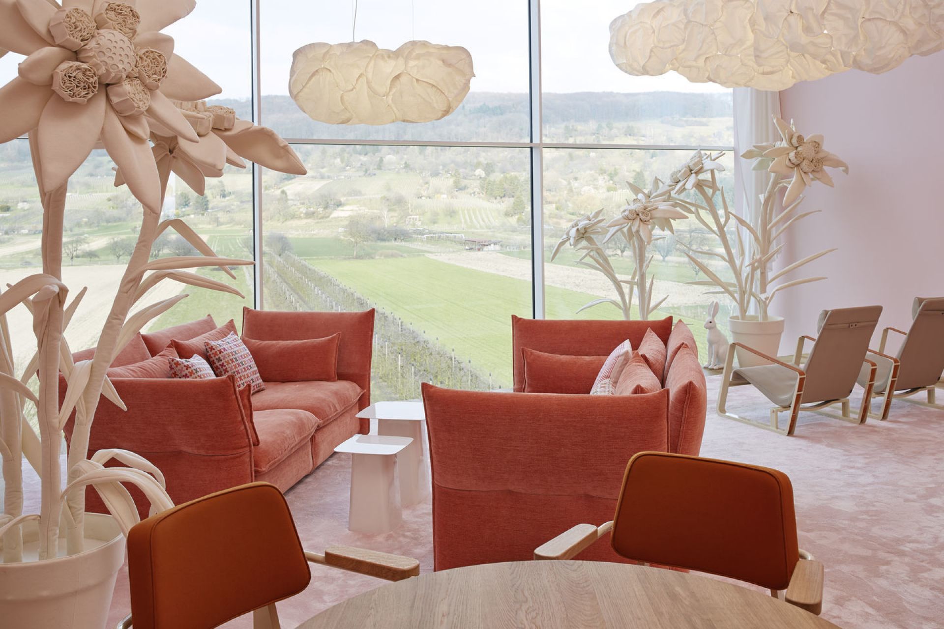 Innenraum mit orangefarbenem Vitra Sessel Fauteuil Direction, Sofa, Sesseln und Blick auf eine grüne Landschaft.