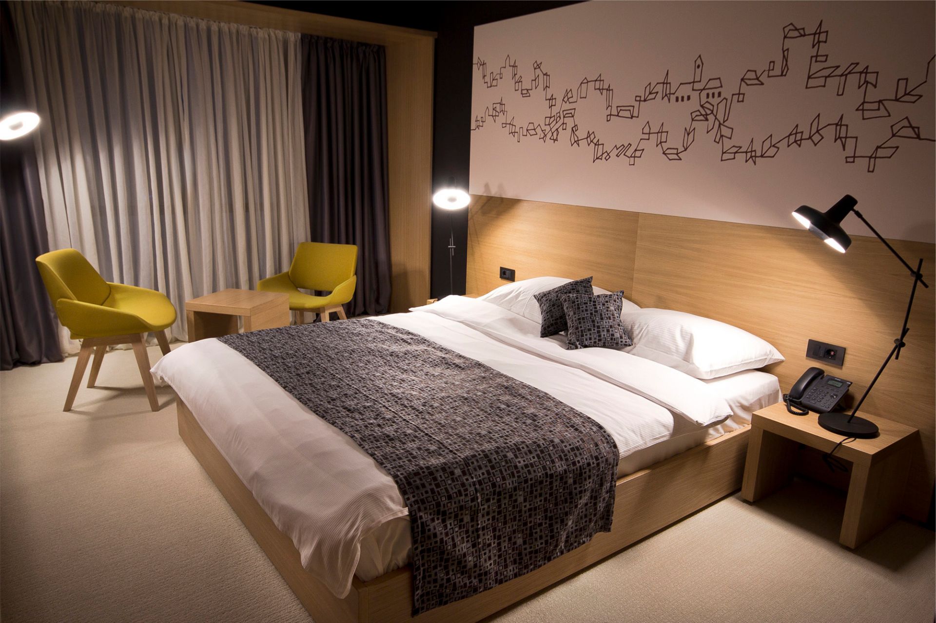 Schlafzimmer mit Doppelbett, zwei gelben Stühlen und einer Arigato Tischleuchte von Grupa, die warmes Licht spendet.