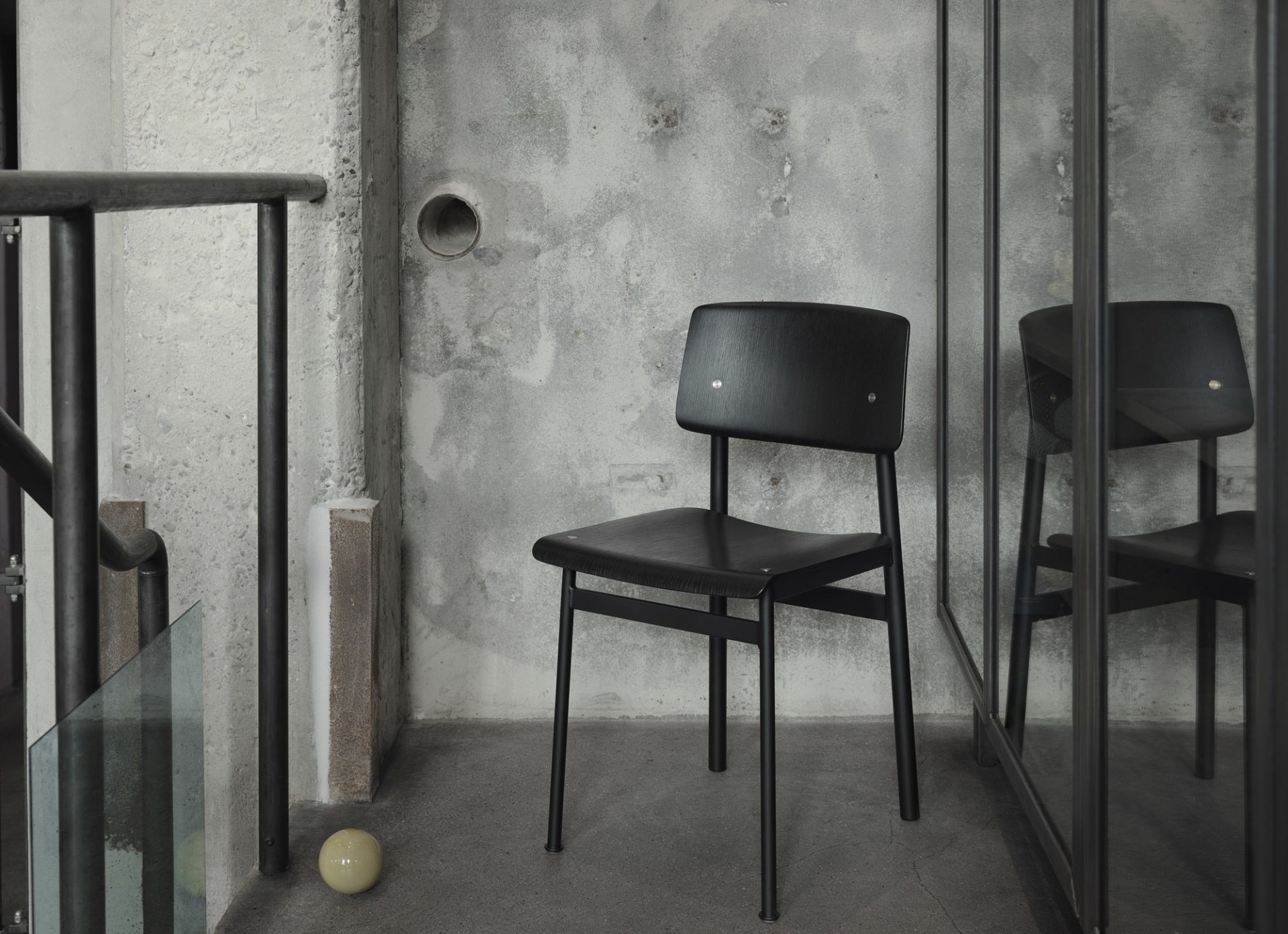 Schwarzer Loft Chair Stuhl von Muuto vor einer grauen Betonwand und Treppe.