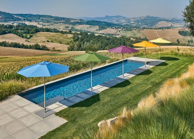 Weishäupl Klassiker Sonnenschirme in verschiedenen Farben am Pool mit idyllischer Landschaft im Hintergrund.