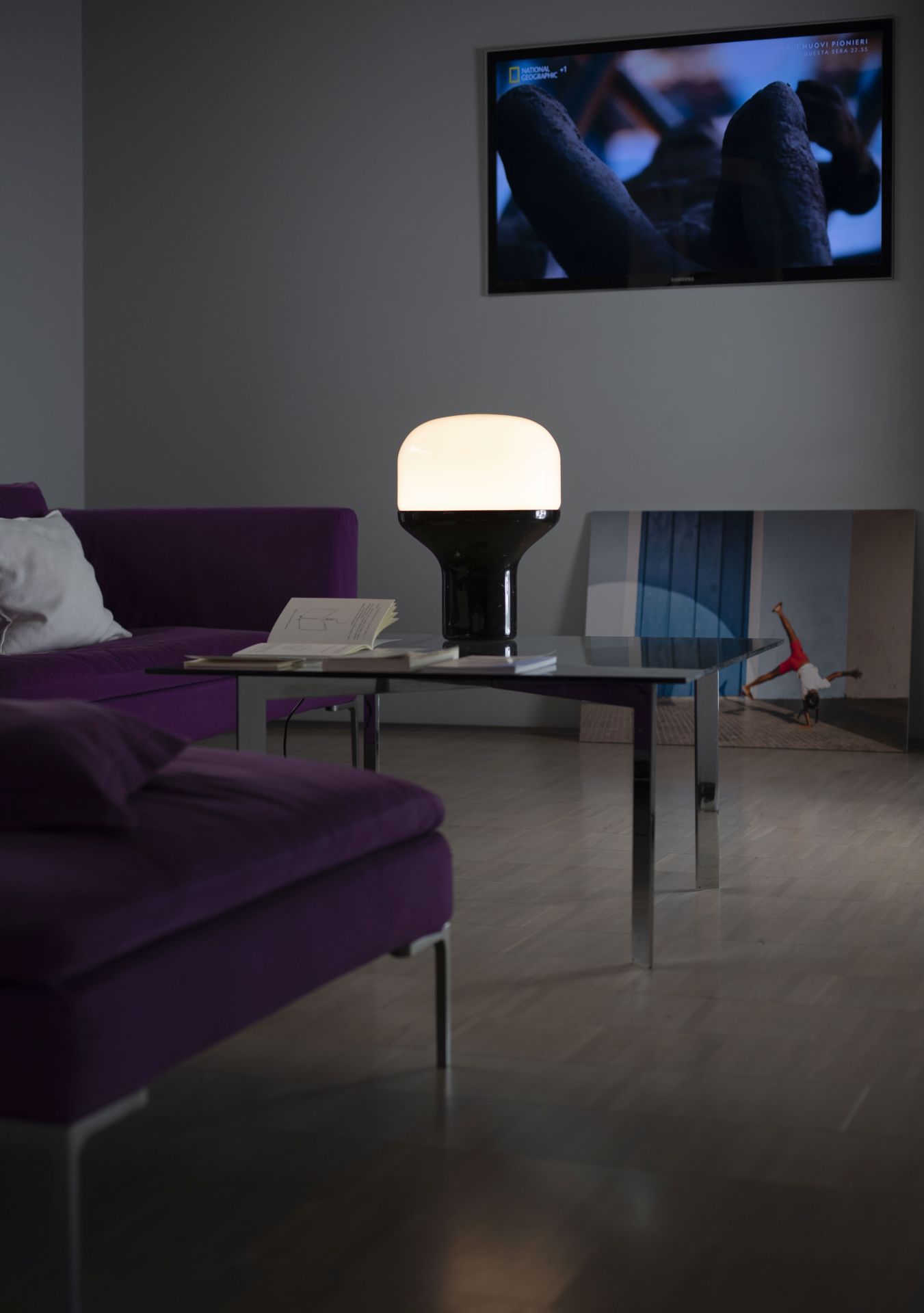 Delux Martinelli Luce Tischleuchte auf einem Tisch im Wohnzimmer mit lila Sofa und TV.