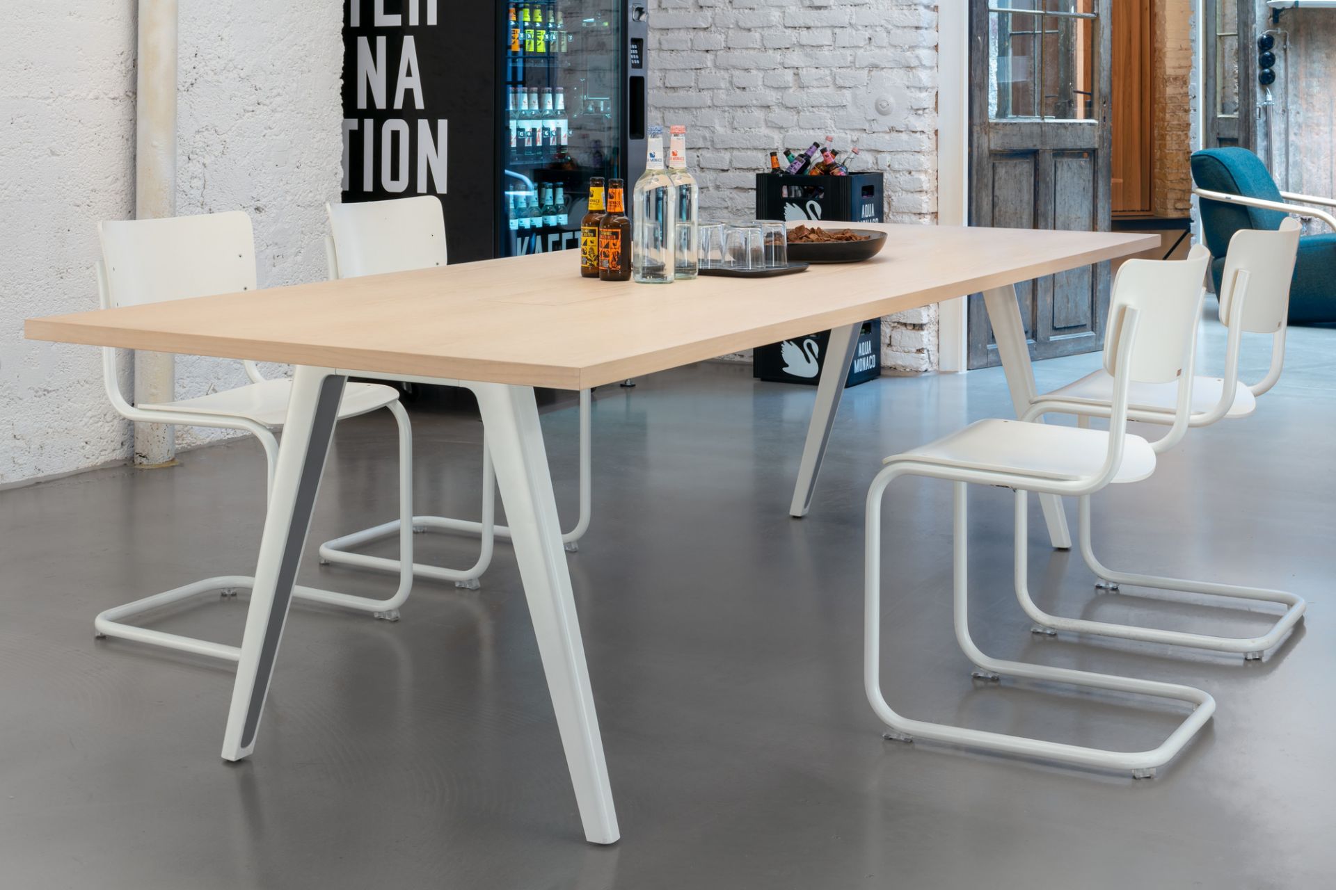 Heller Thonet Tisch 1500 mit Getränken und Snacks, umgeben von weißen Freischwinger Stühlen im modernen Büro.