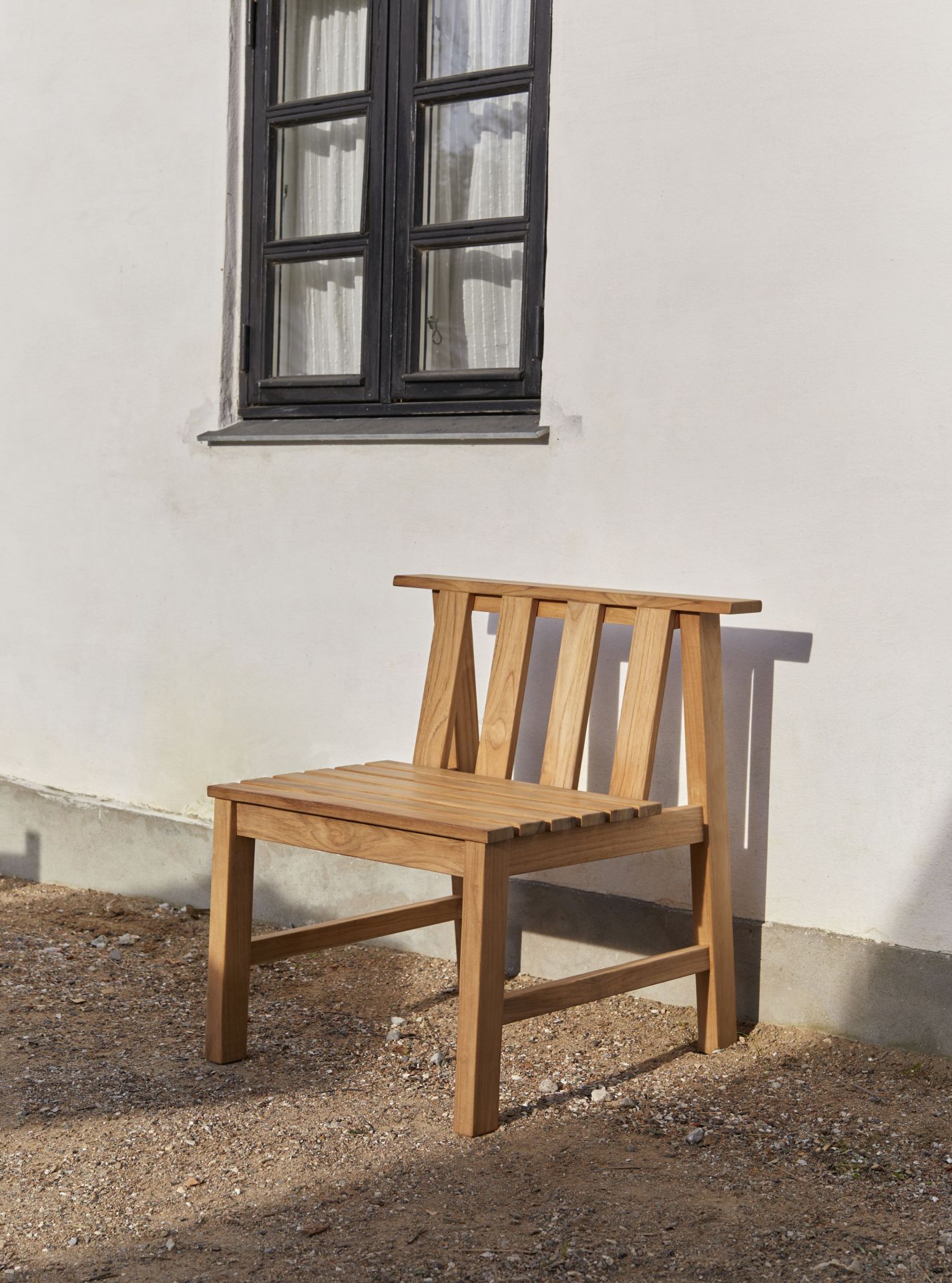 Cadence Stuhl Teak Outdoor von Skagerak by Fritz Hansen vor weißer Hauswand mit Fenster.
