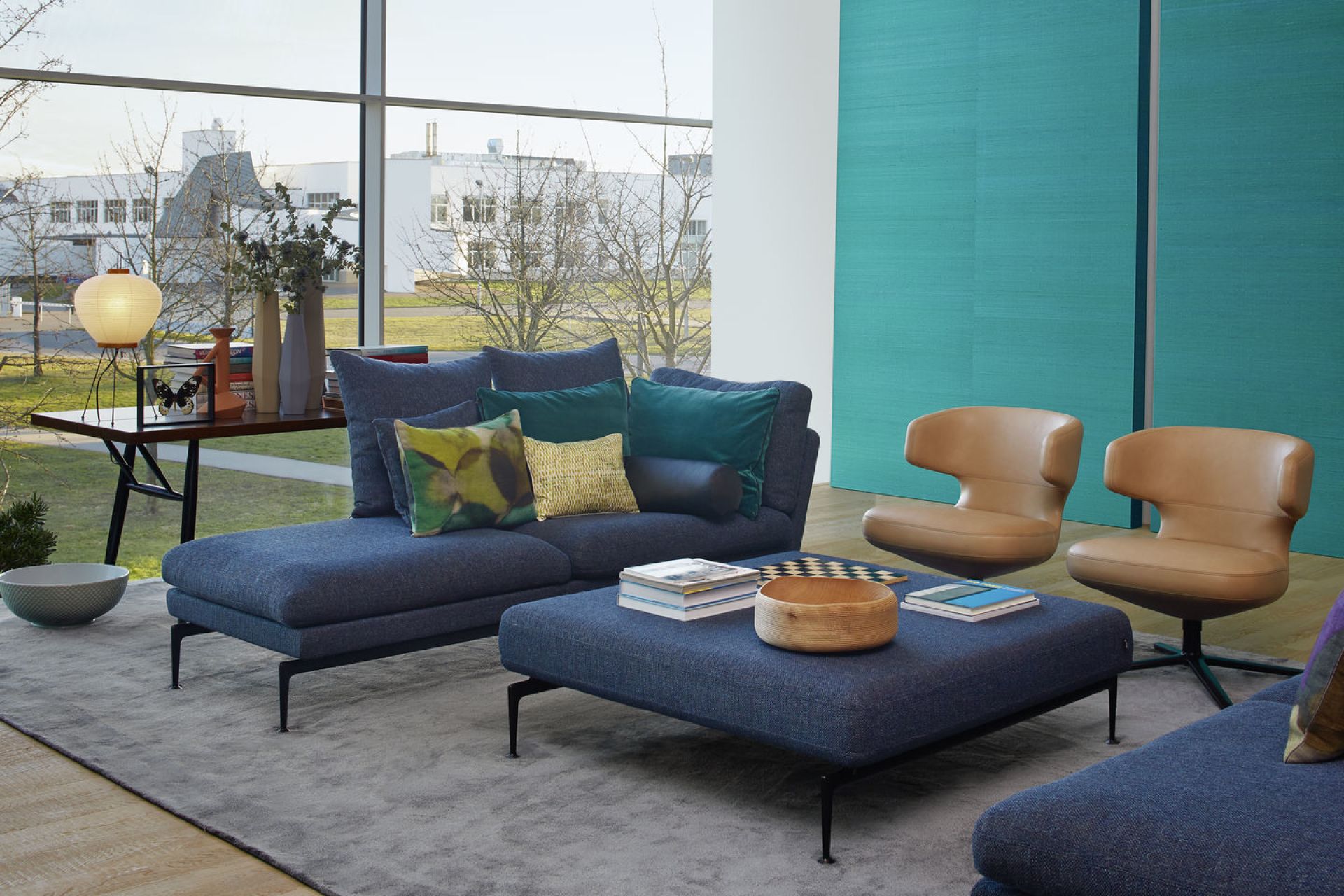 Wohnzimmer mit blauem Sofa, Ottomanen und zwei Sesseln vom Typ Vitra Petit Repos in Leder.