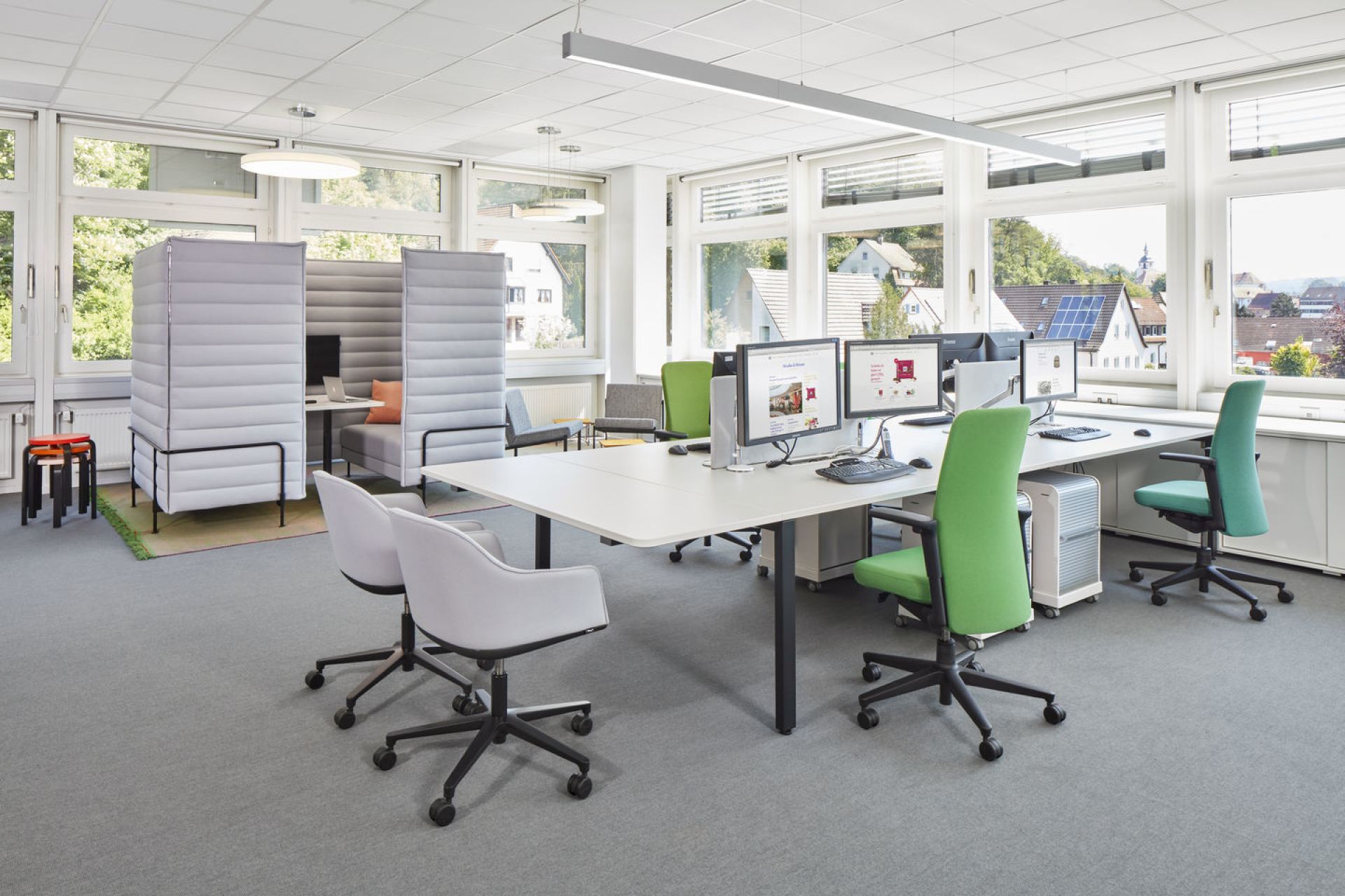 Helles Büro mit weißen Schreibtischen, Computern und grünen sowie grauen Vitra Softshell Drehstühlen.