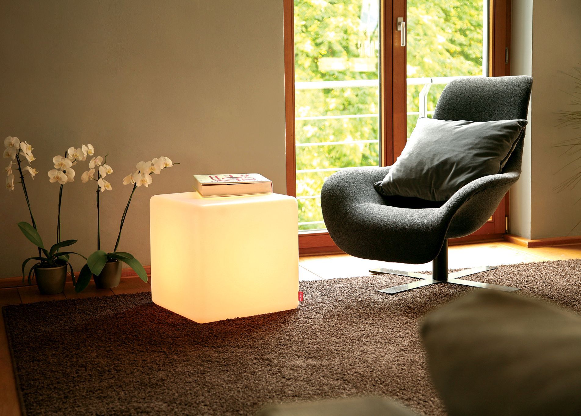 CUBE Hocker leuchtend weiß als Beistelltisch mit Buch im Wohnzimmer.