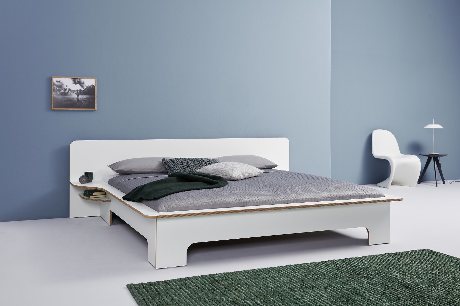 Weißes Plane Doppelbett von Müller Möbelwerkstätten mit Nachttisch und grauer Bettwäsche.