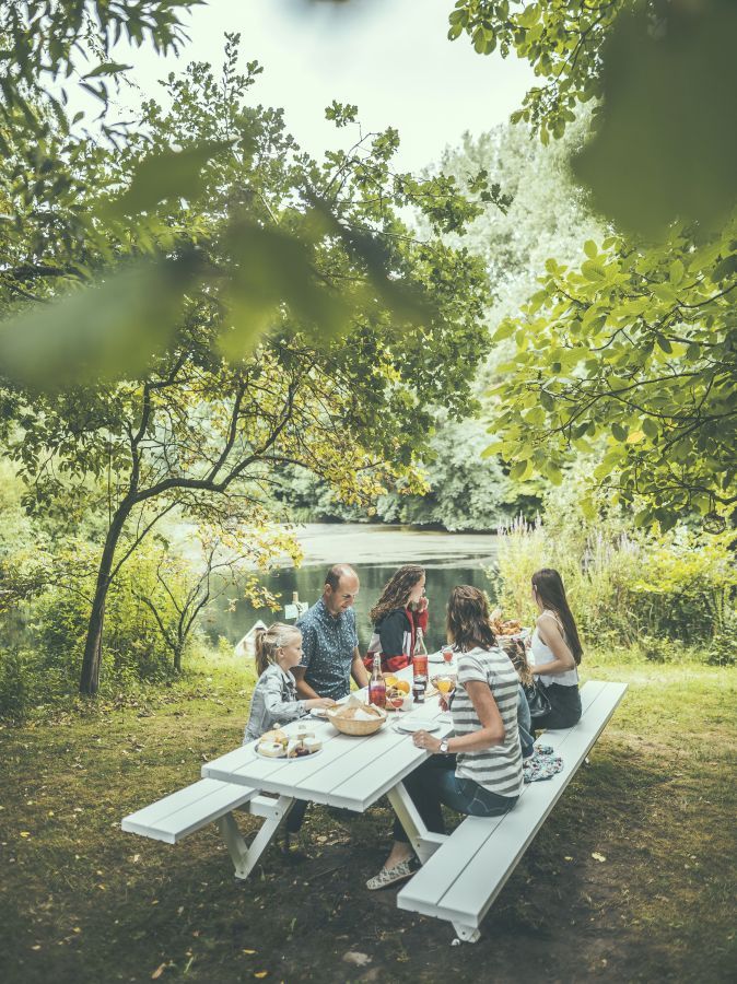Familie genießt Picknick am weißen Extremis Marina Picknicktisch mit Bänken im Grünen.