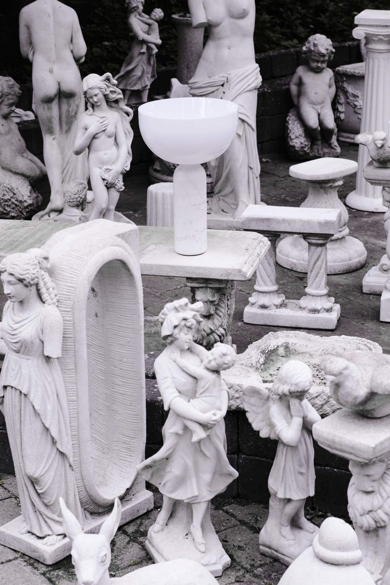 Weiße Kizu Tischleuchte von New Works zwischen Statuen. Design Lampe für Wohnzimmer und Schlafzimmer.