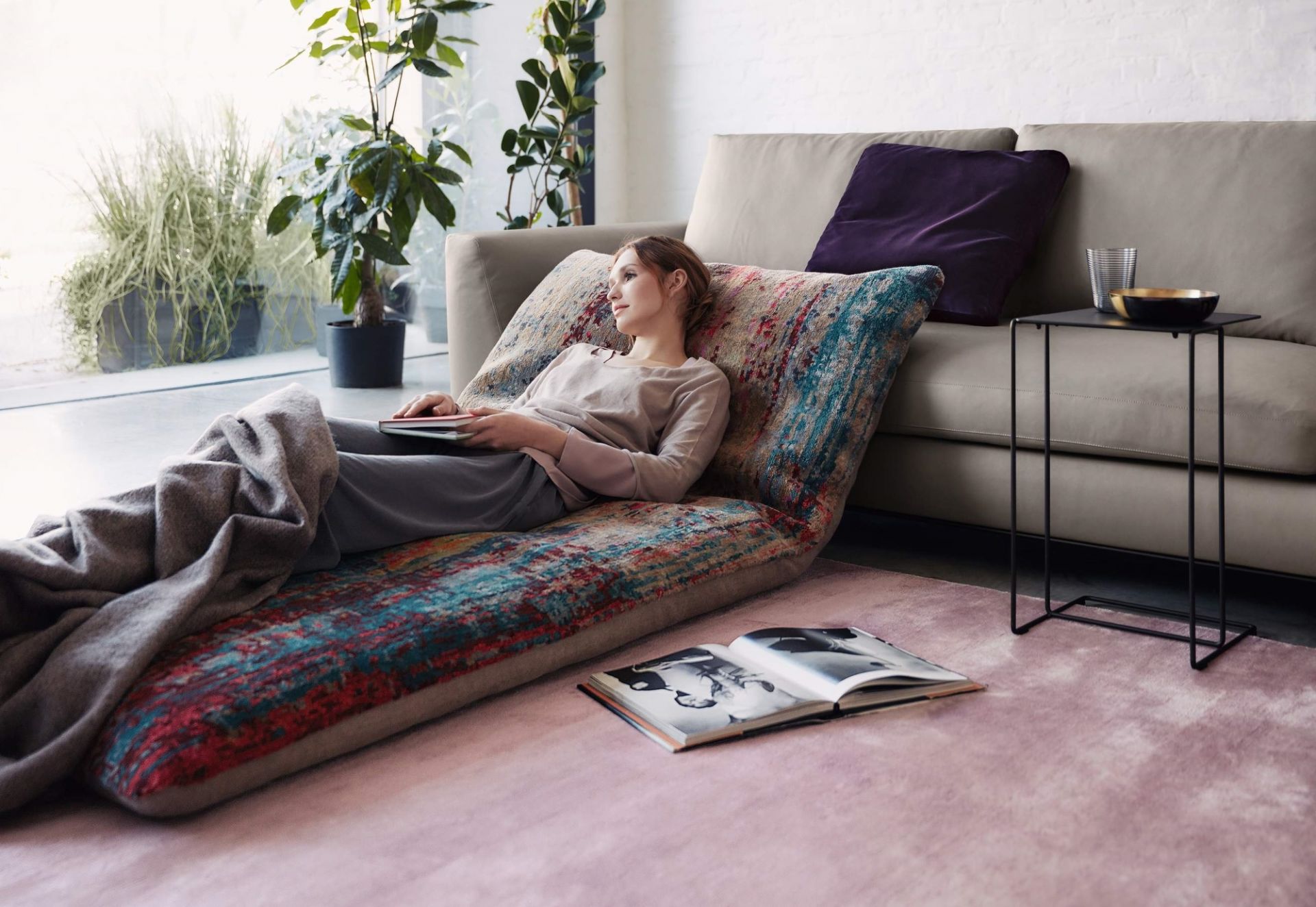 Frau entspannt auf Sofa neben Walter Knoll Beistelltisch mit Getränken, Buch und Zimmerpflanzen im Wohnzimmer.