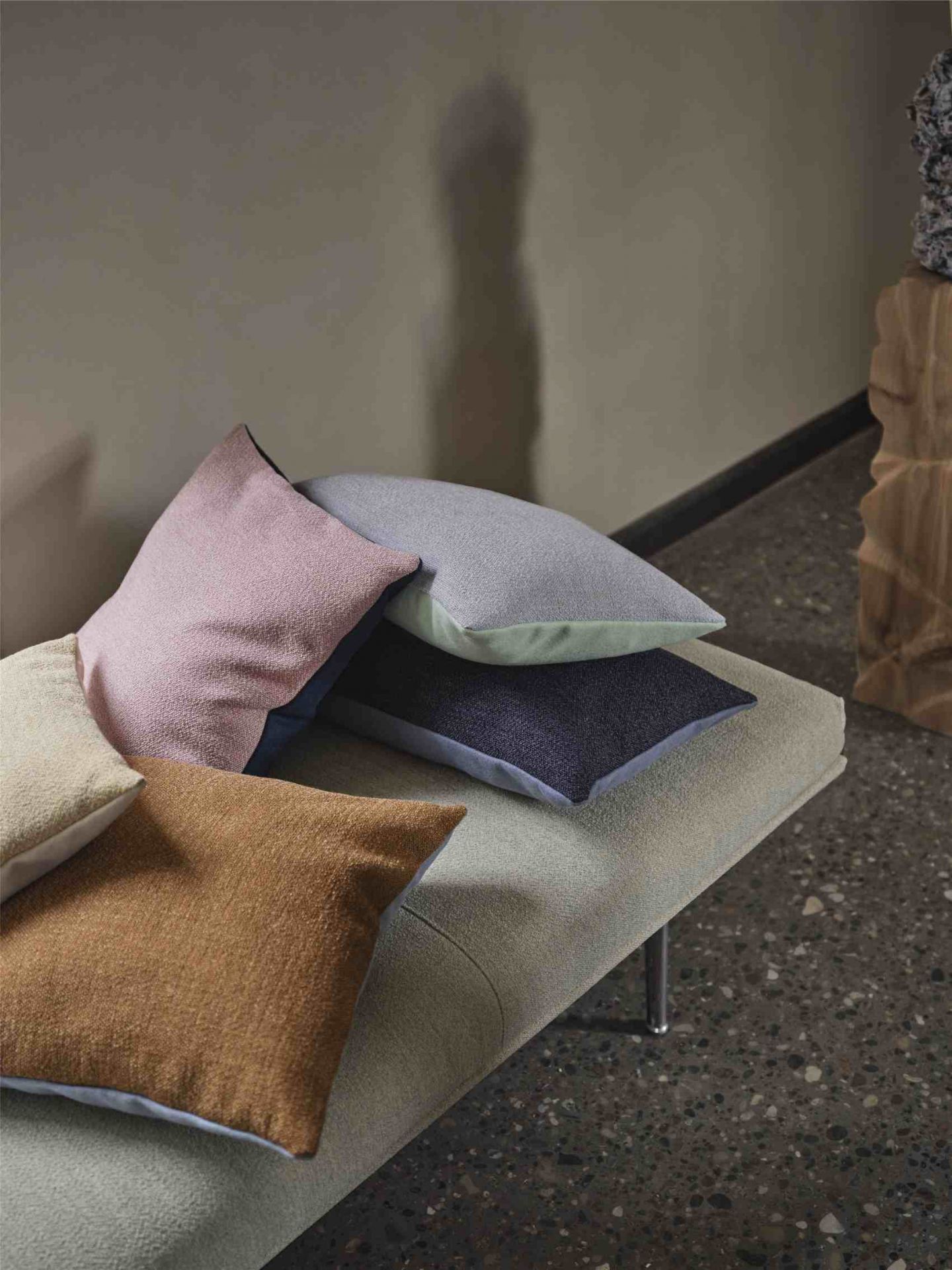 Mehrere farbige Muuto Mingle Cushion Kissen aus Stoff liegen auf einer gepolsterten Bank.