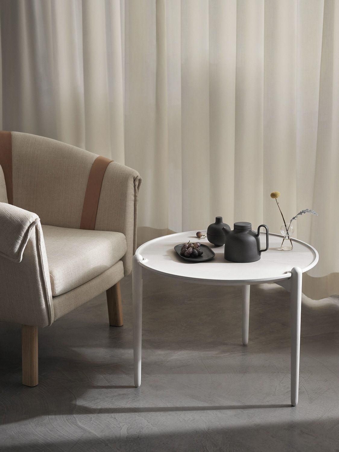 Aria Table Beistelltisch von Design House Stockholm neben Sessel mit Deko-Objekten auf grauem Untergrund.
