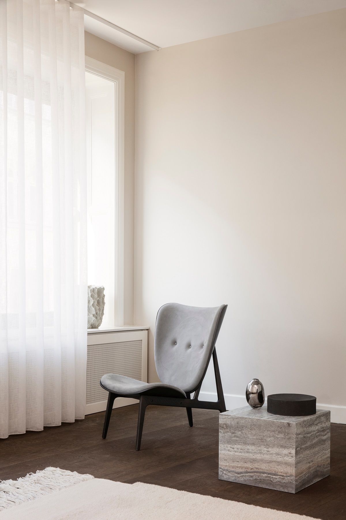 Heller Raum mit NORR11 Elephant Lounge Chair Sessel in Grau, Beistelltisch und Vorhang.