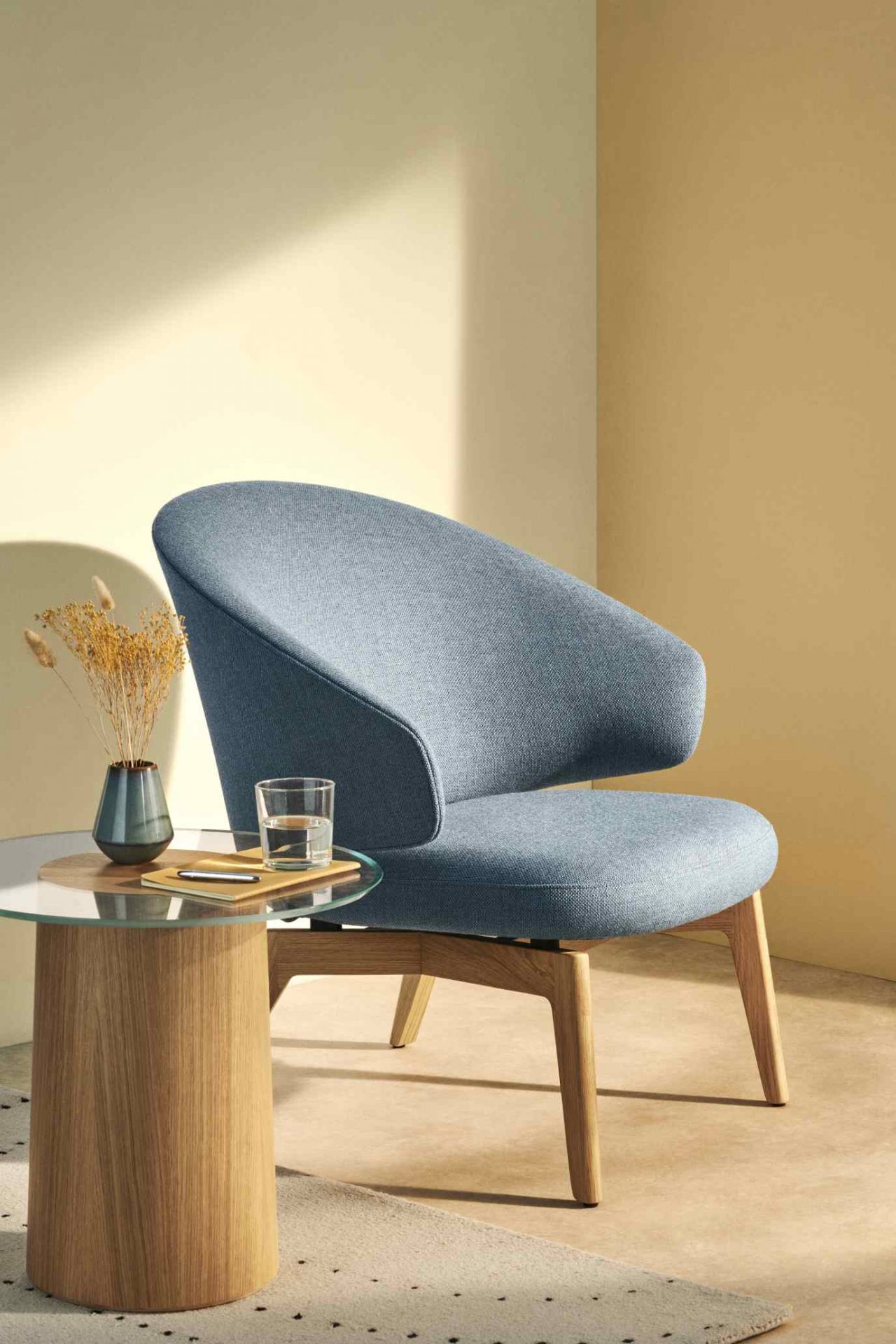 Blauer Fritz Hansen Let Sessel mit Holzbeinen neben einem Beistelltisch mit Glasplatte.