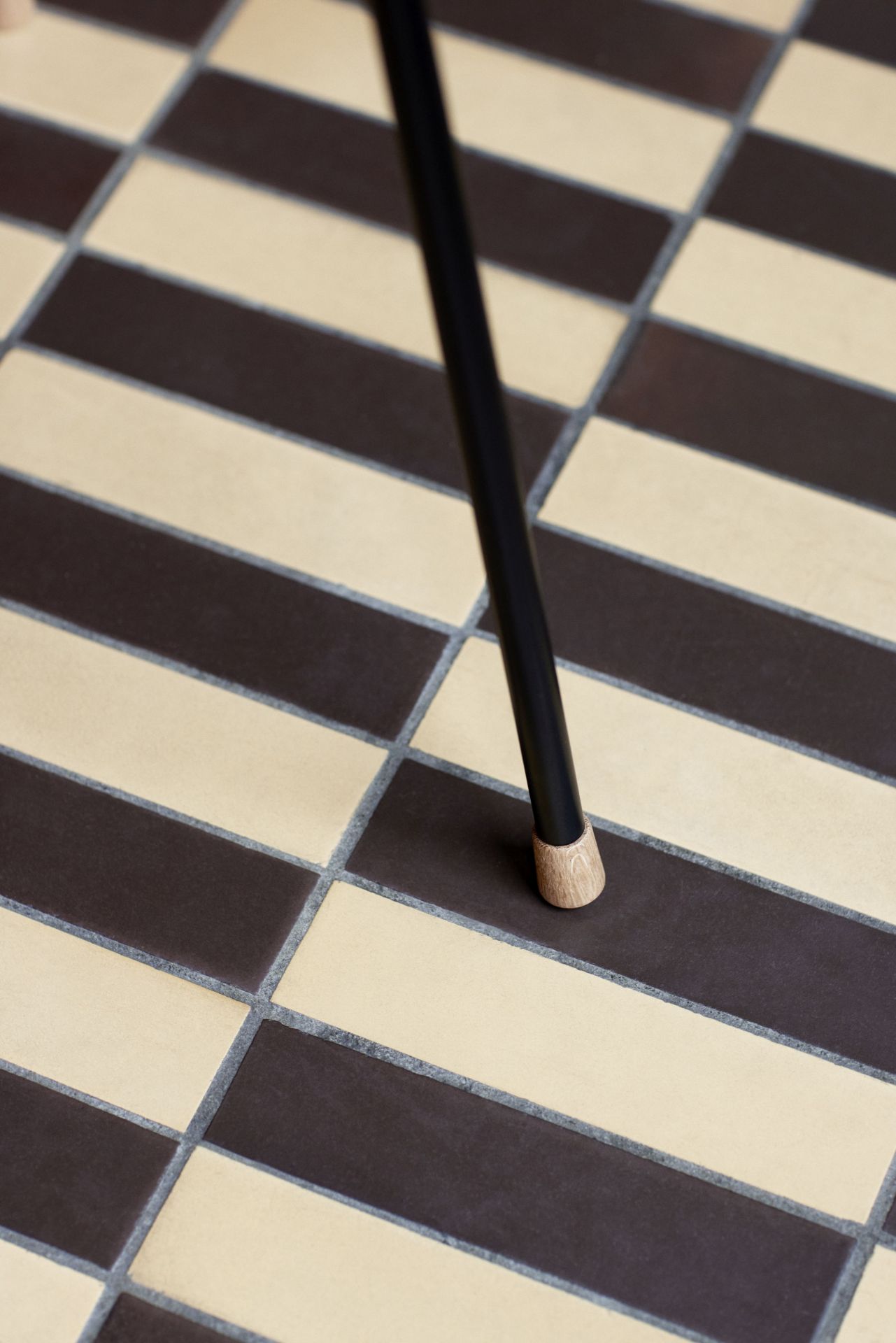Detailaufnahme vom Bein des Carl Hansen Vega Stuhls auf einem Schachbrettmuster-Fliesenboden.