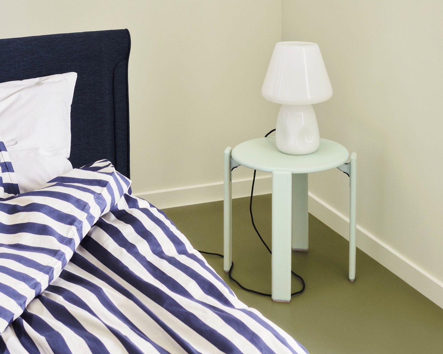 Heller mintfarbener Rey Stool Hocker von Hay als Nachttisch mit Lampe neben einem Bett.