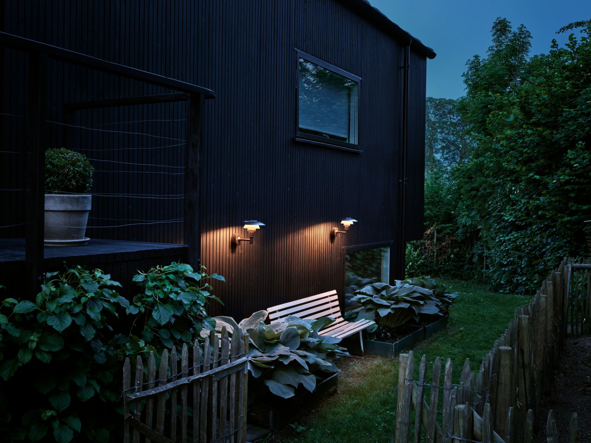 Außenaufnahme: PH 3 - 2 1/2 Wandleuchte von Louis Poulsen beleuchtet Garten mit Bank.