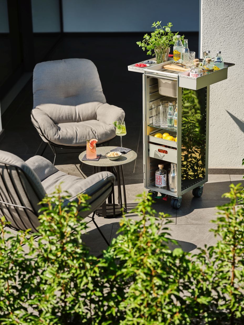 Rivet Rocker Flugzeugtrolley Bordbar: Silberner Servierwagen mit Getränken und Gläsern auf einer Terrasse.