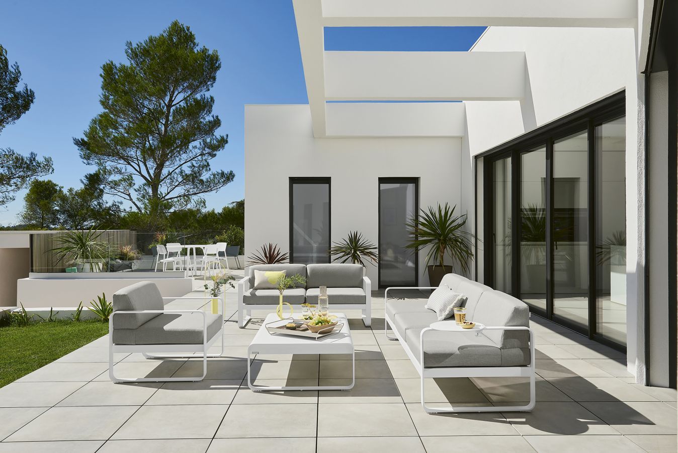 Bellevie Outdoor-Lounge-Set mit großem, niedrigem Tisch von Fermob in Weiß und Grau auf einer Terrasse.