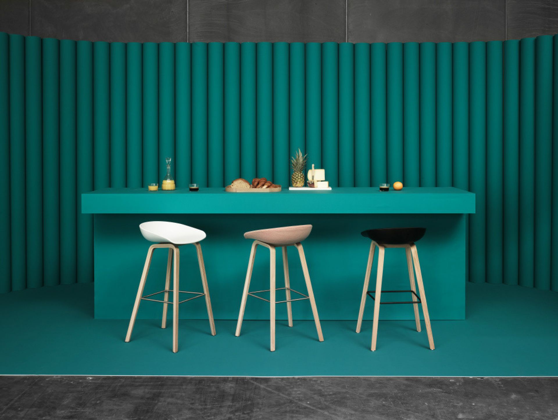 Drei Hay About a Stool AAS32 Barhocker in Weiß, Beige und Schwarz vor türkisfarbenem Hintergrund.