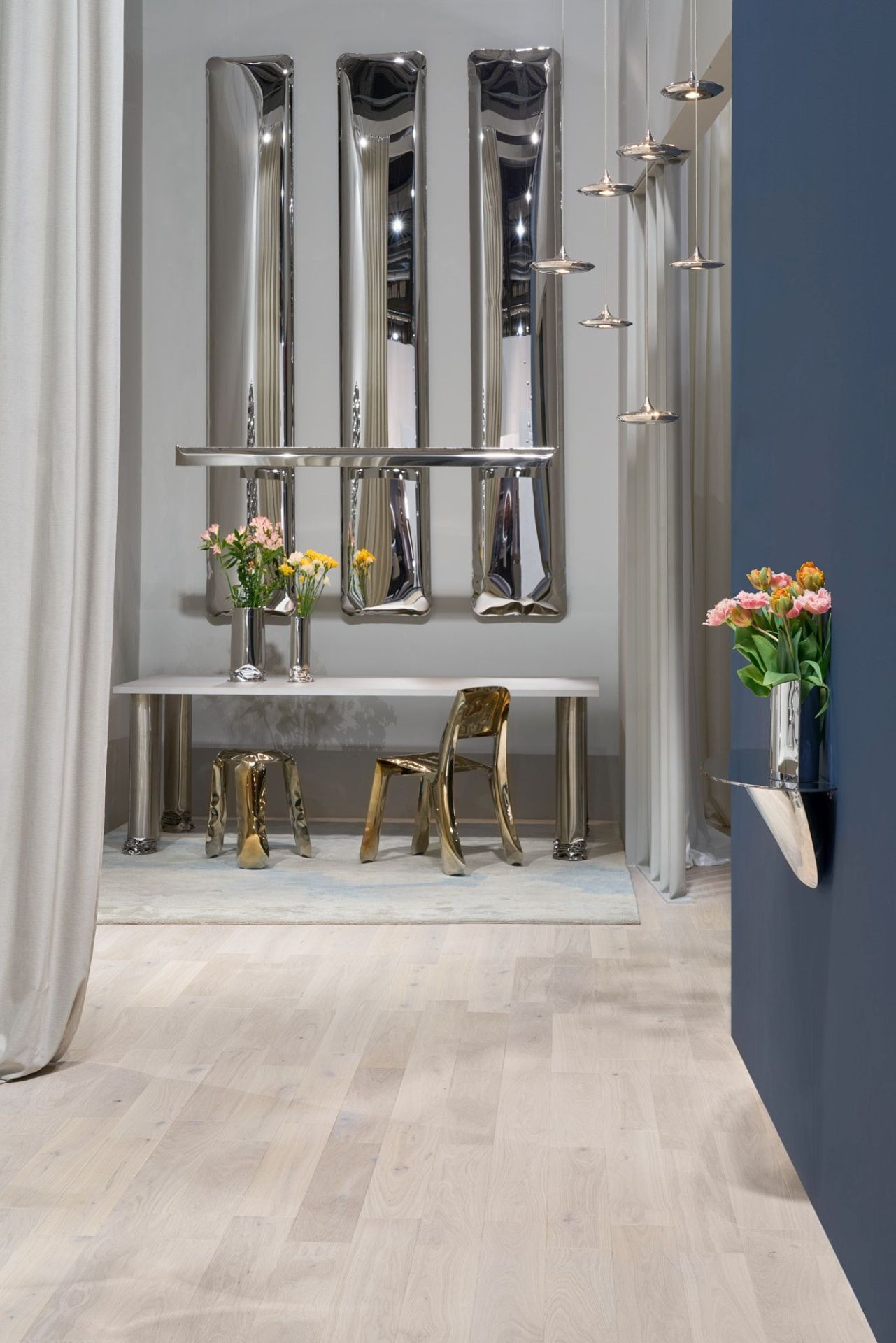 Tafla Q Spiegel von Zieta: Drei silberne, längliche Design-Spiegel über einem Tisch mit Blumenvasen und goldenen Stühlen.