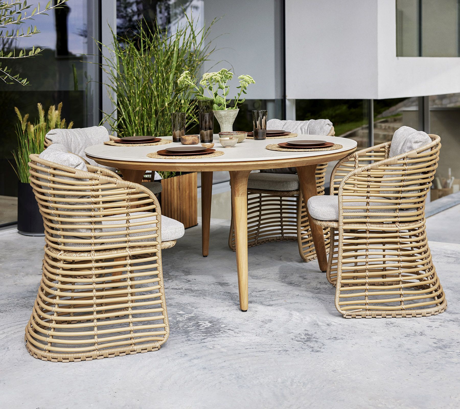 Bild eines Cane-Line Basket Sessels aus Rattan mit Esstisch und Stühlen im Außenbereich.