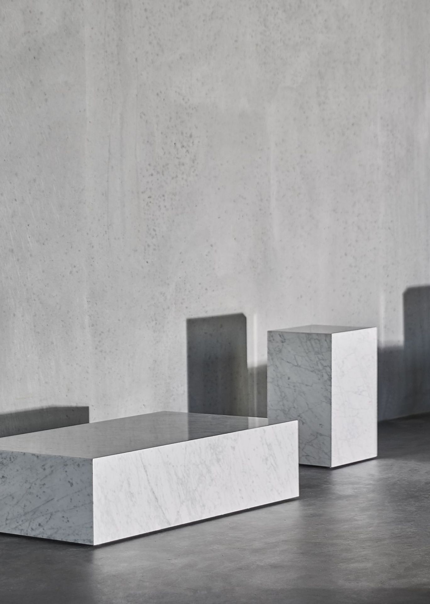 Audo Plinth Cubic Beistelltisch aus Marmor, rechteckig und quadratisch, vor grauer Wand.