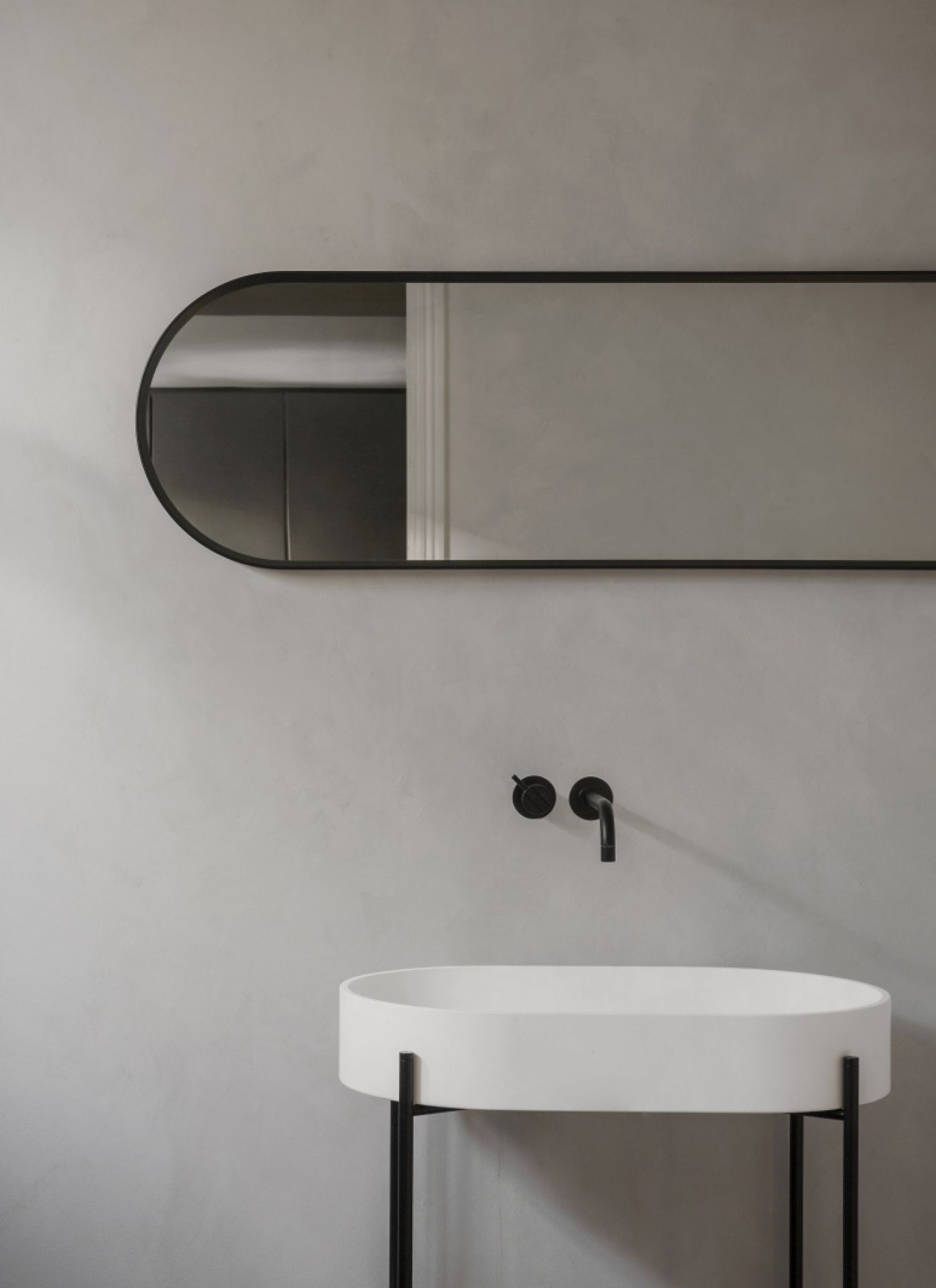 Norm Wall Mirror Oval von Audo: Ovaler Wandspiegel mit schwarzem Rahmen über einem weißen Waschbecken.
