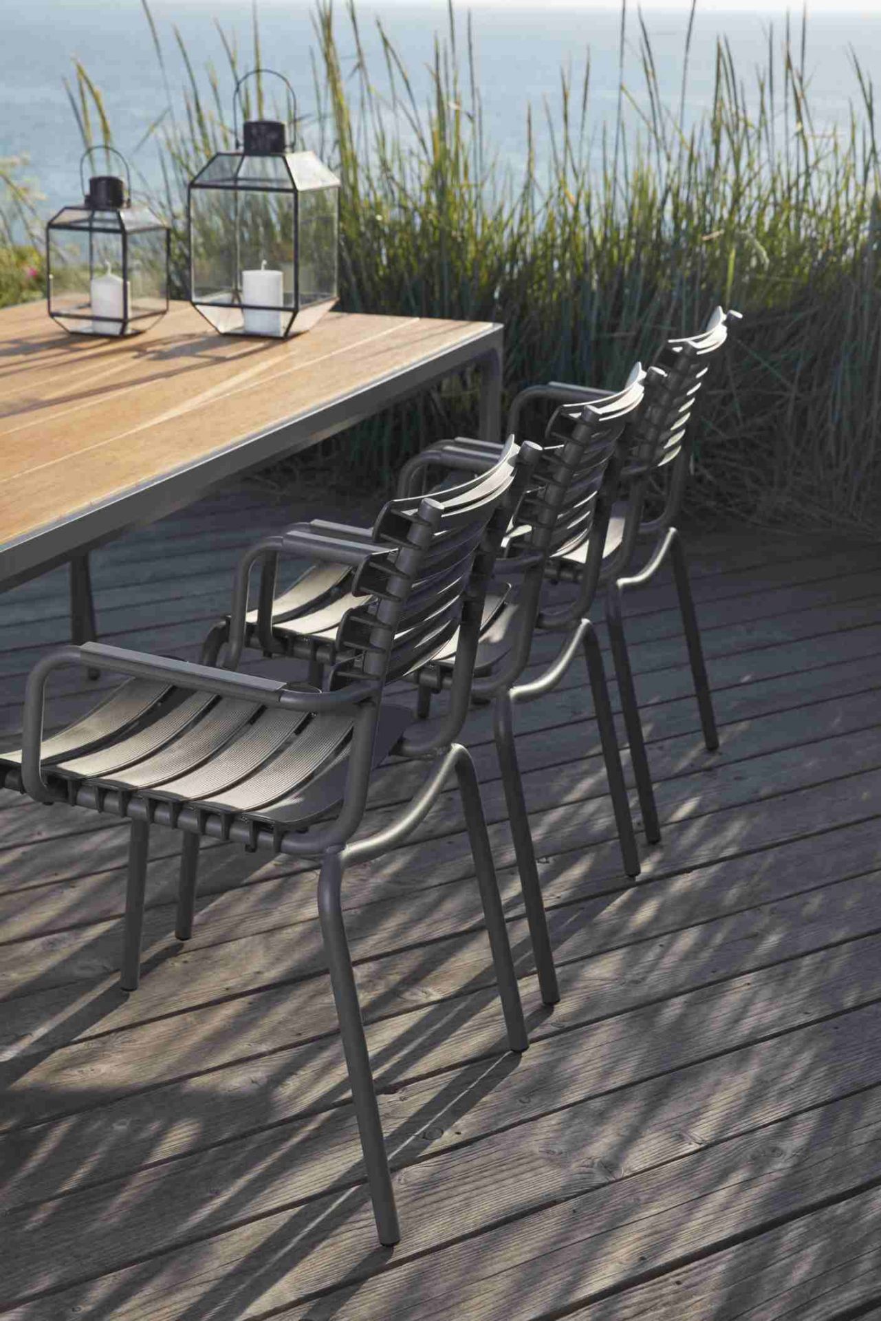 Houe Four Esstisch Outdoor mit Stühlen und Windlichtern auf einer Holzterrasse am Meer.