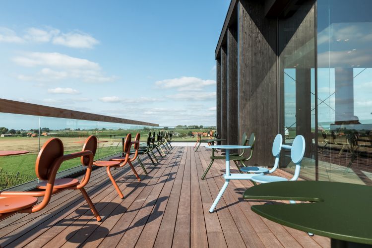 Extremis Bistroo Stühle und Tische in verschiedenen Farben auf einer Holzterrasse mit Ausblick.