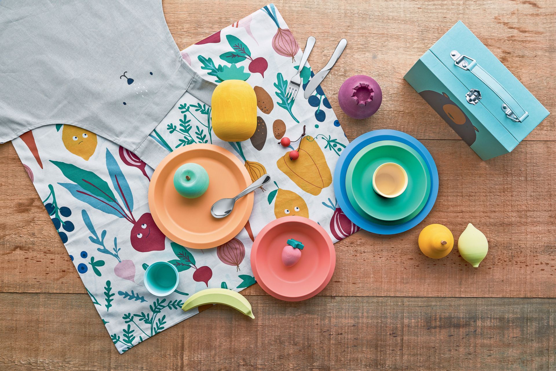 Buntes Alessi Kindergeschirr "Giro Kids Collection" in Orange, Blau und Grün auf Holztisch mit Stoffserviette.